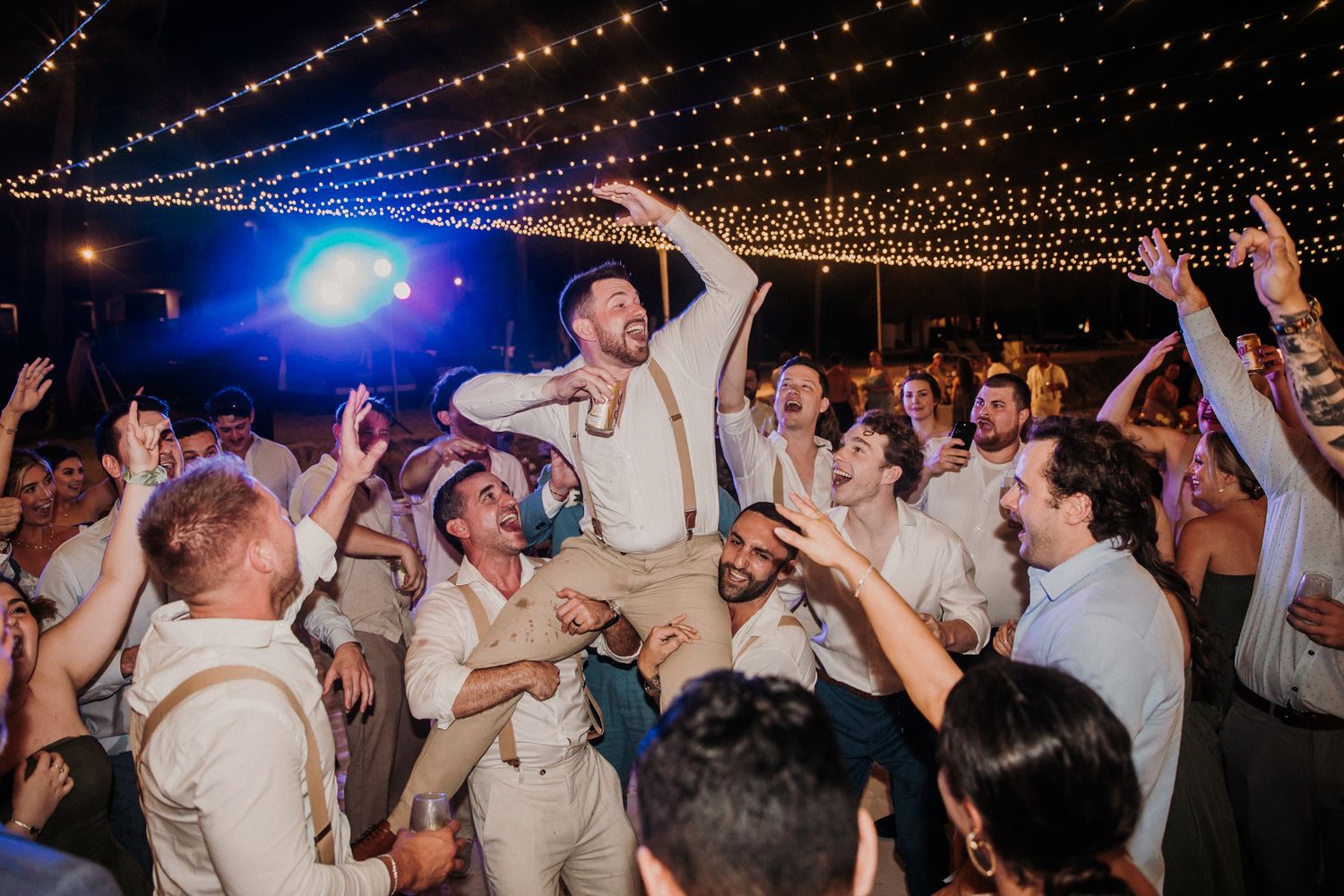 Wedding celebration with crowd dancing under string lights at outdoor evening reception party.  El Dorado Royale Wedding Photographer