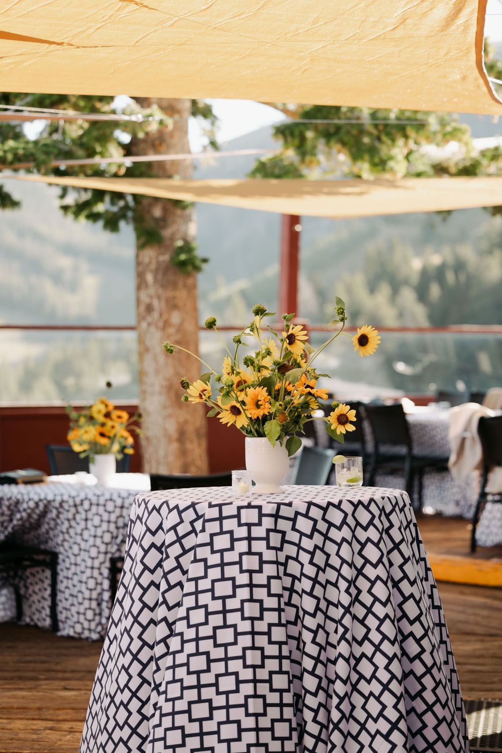 Outdoor event tables with black and white geometric patterned tablecloths decorated with yellow sunflower centerpieces.