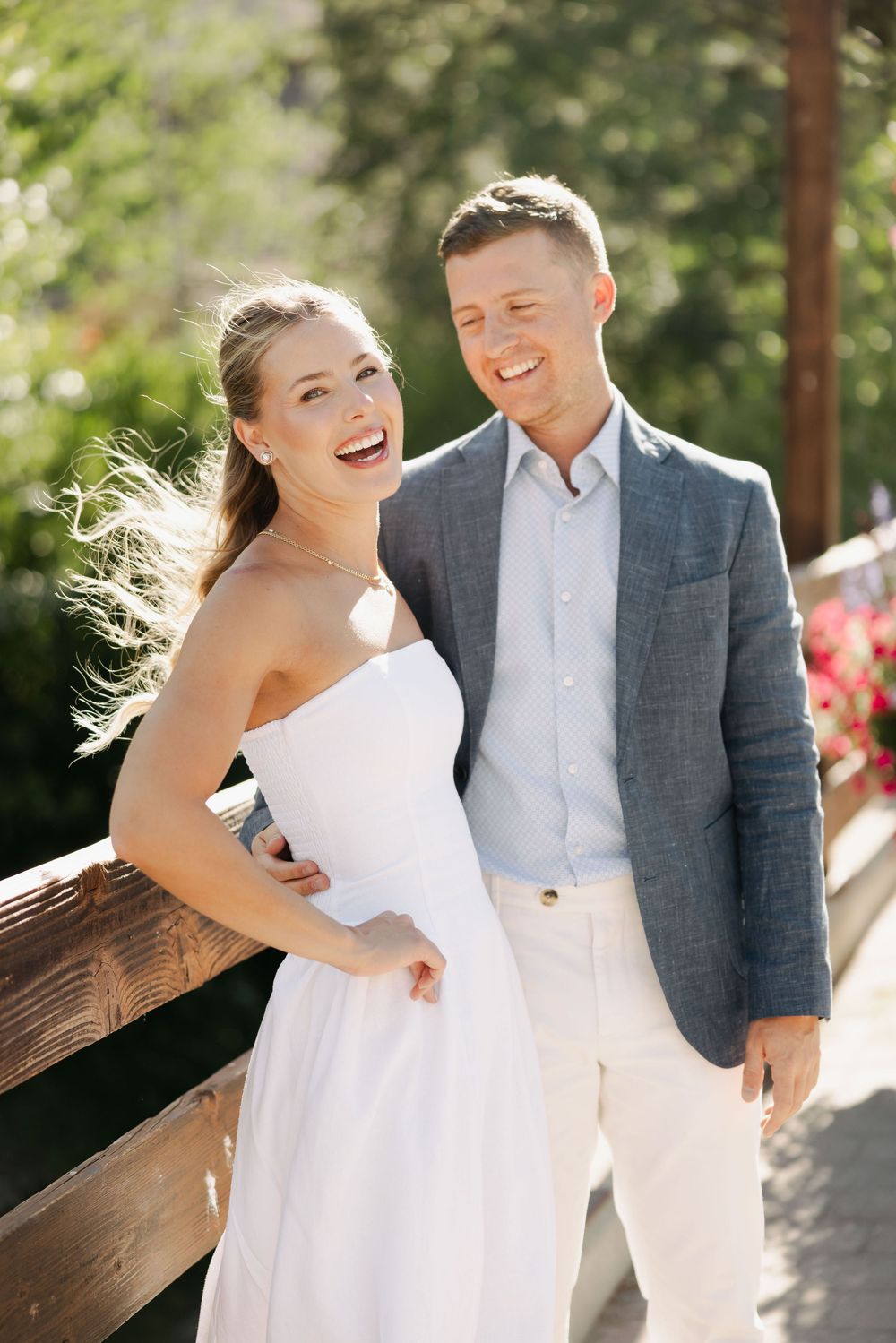 Joyful couple sharing laughter during outdoor wedding photoshoot in bright sunlight.