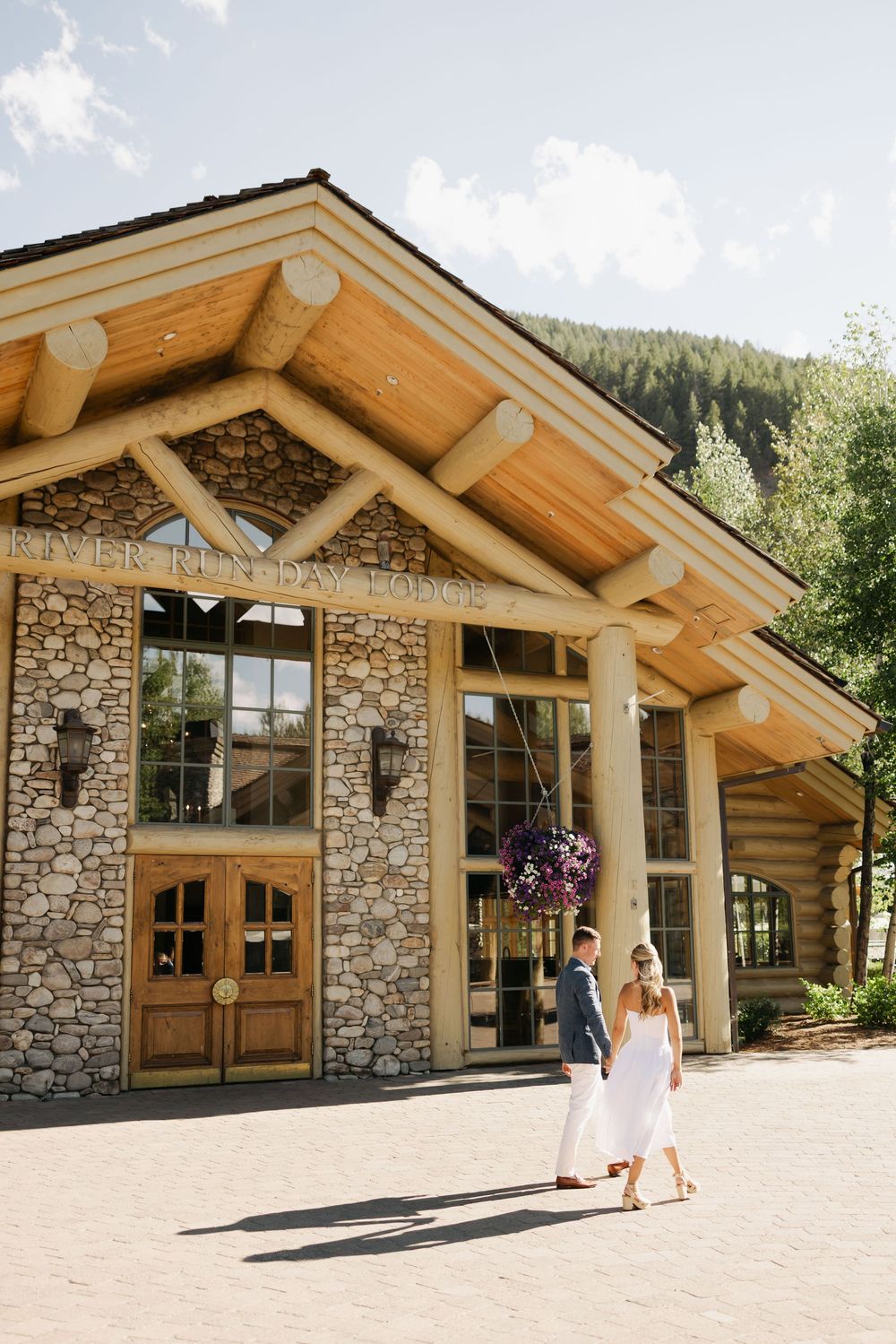 Modern rustic lodge with stone and wood architecture features mountain views and hanging flower baskets.