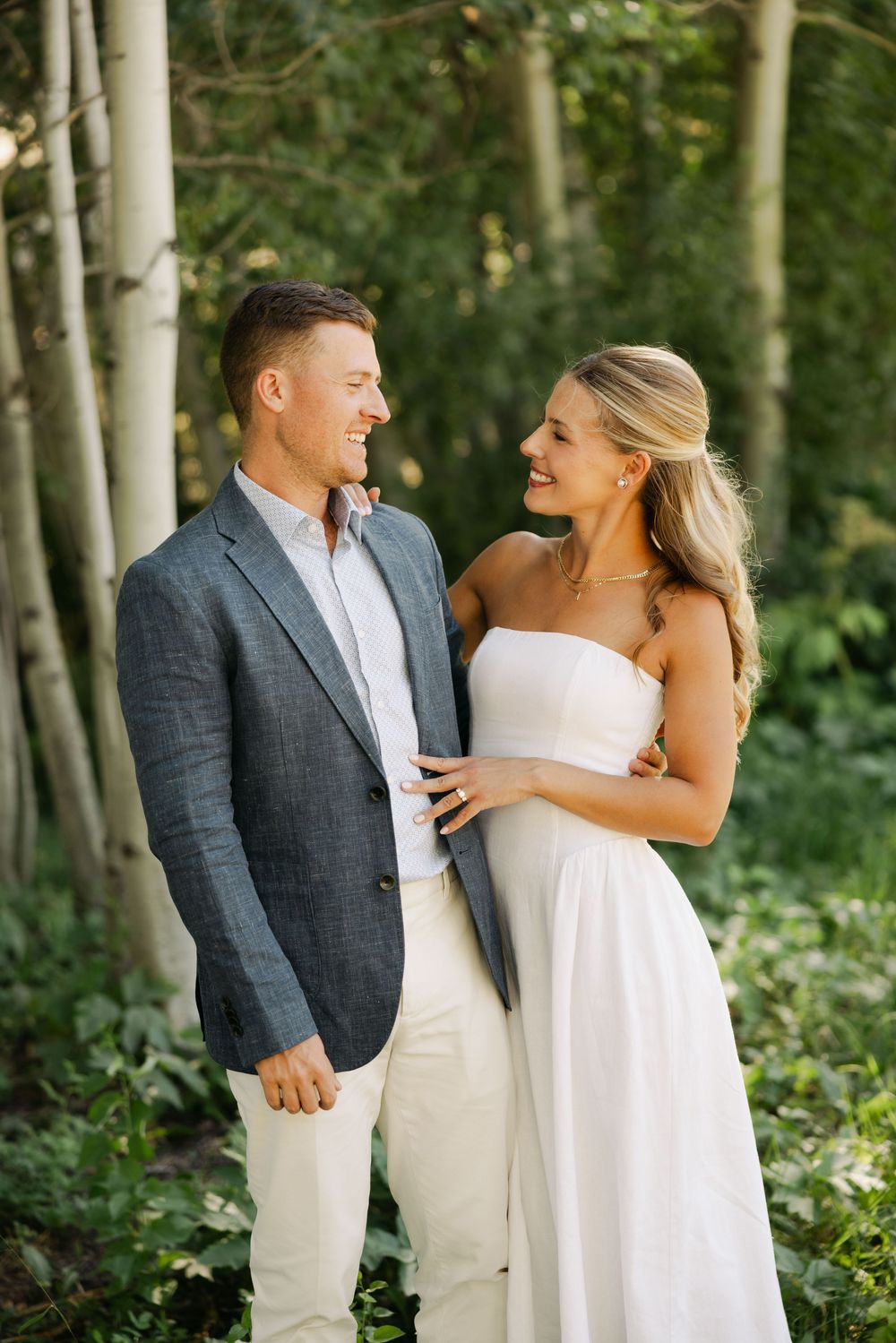 A couple shares a romantic moment among aspen trees in formal wedding attire.
