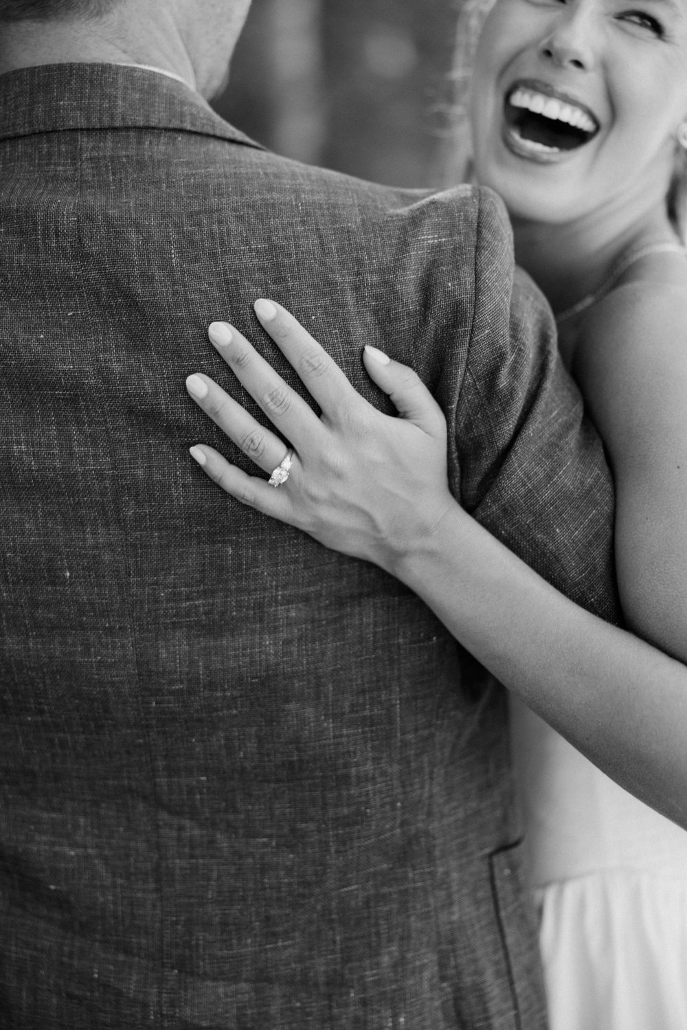 Close-up black and white photo showing hands embracing and a sparkling engagement ring.
