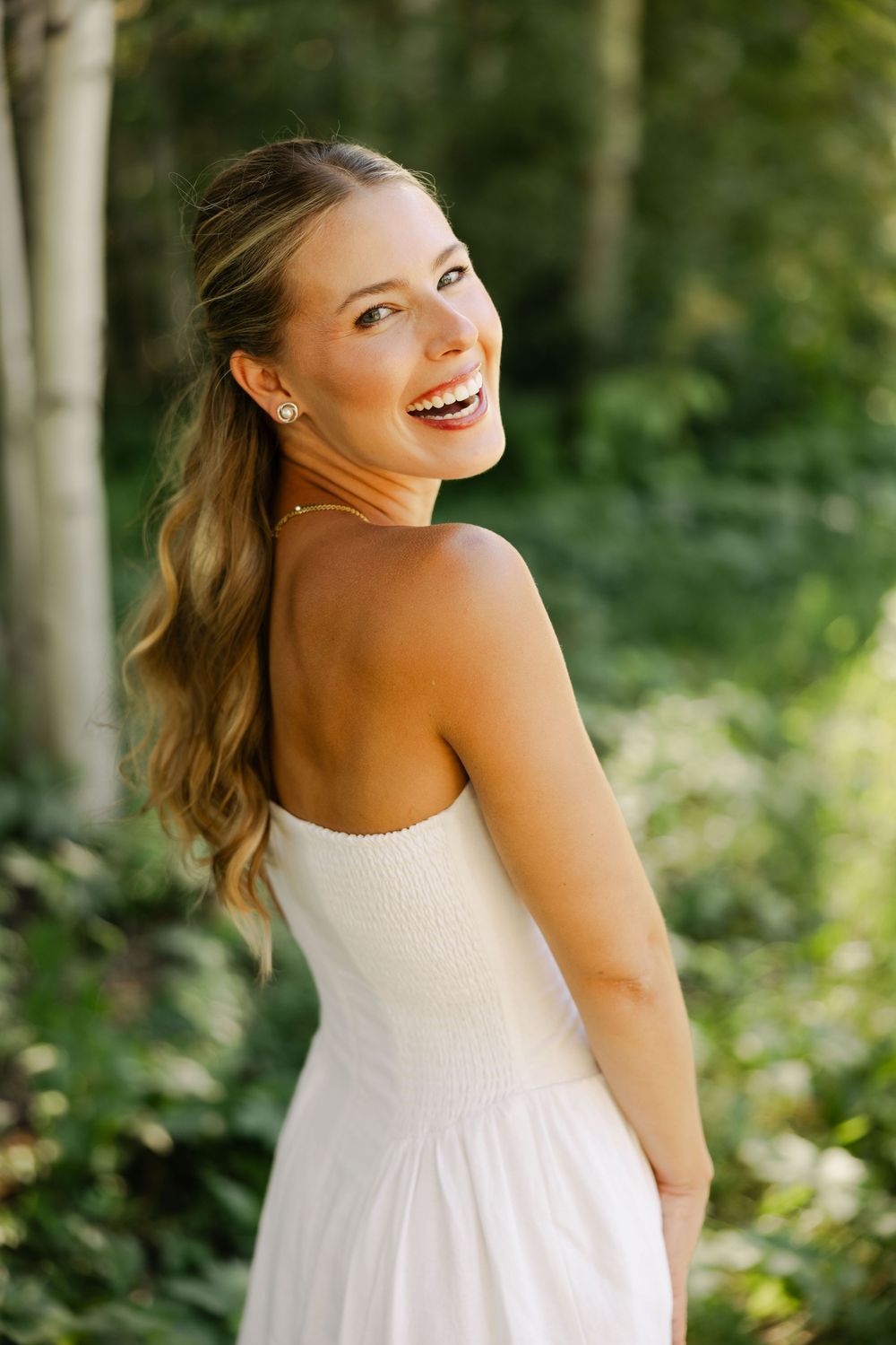 A person in a white summer dress twirls playfully in a forest setting.