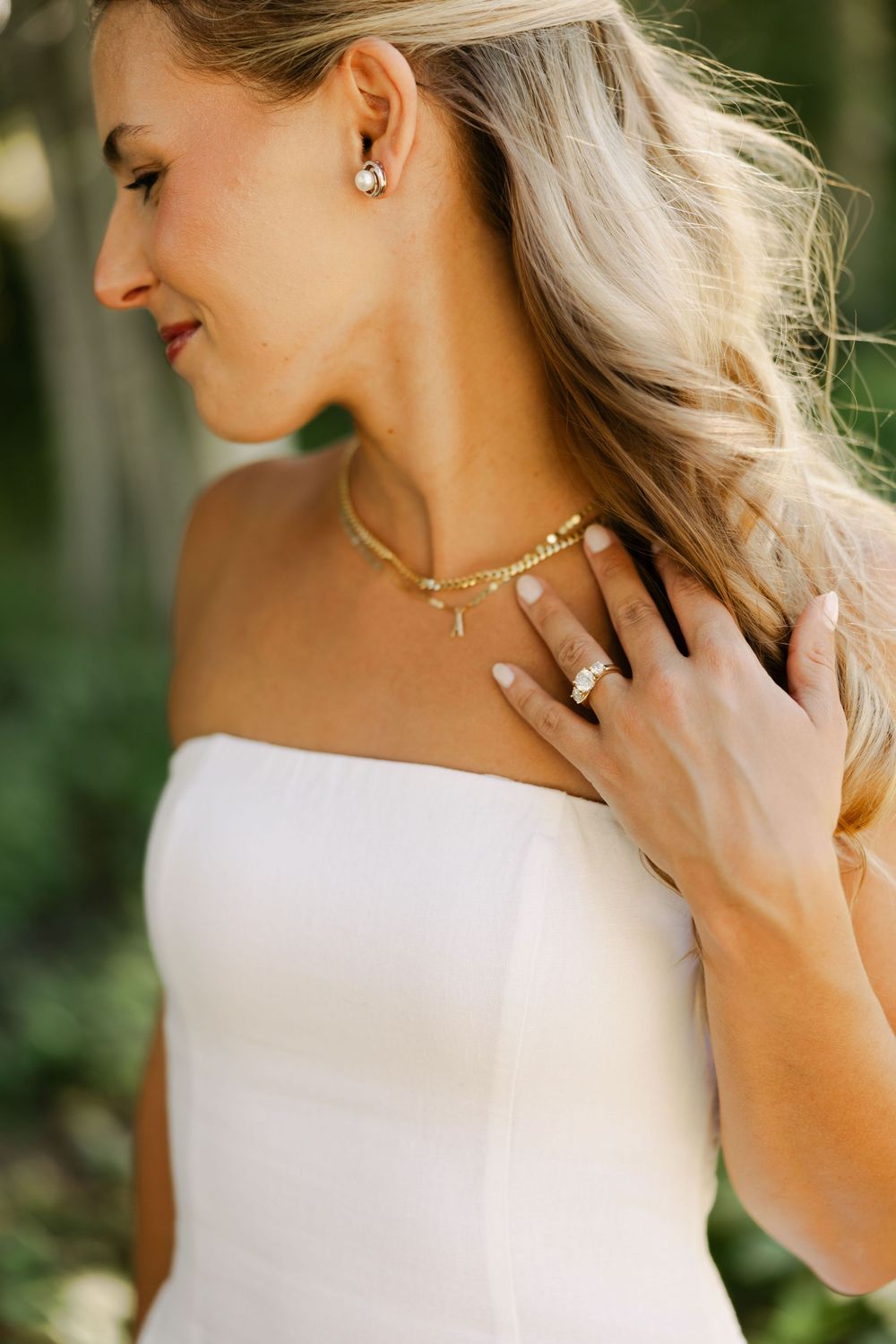Elegant bridal portrait showing delicate jewelry and a white strapless dress against a natural outdoor backdrop.
