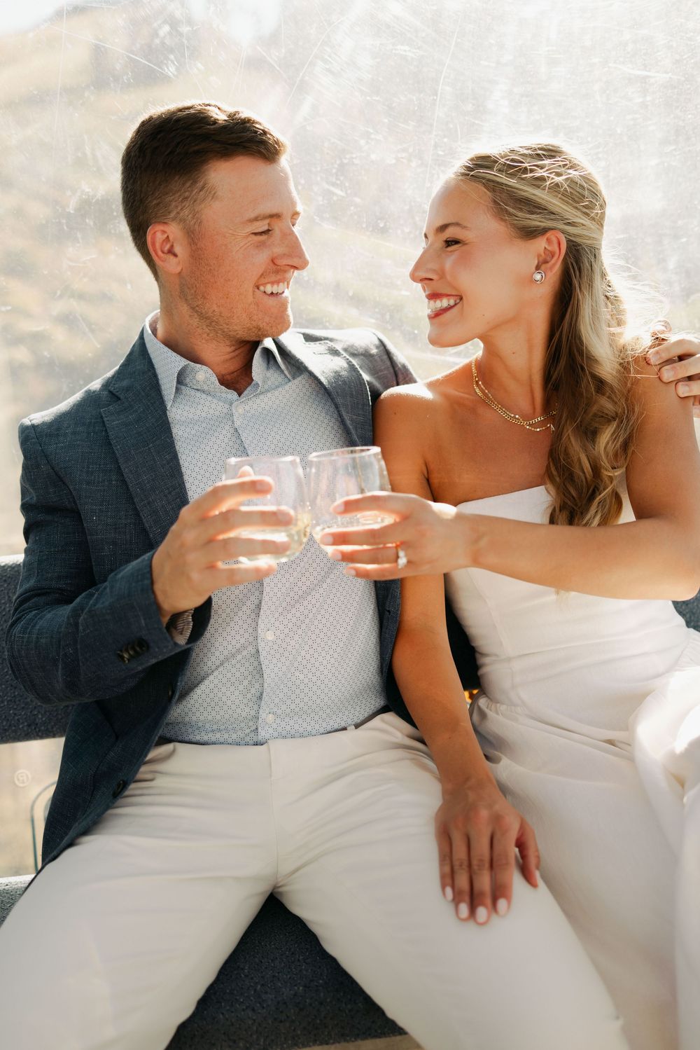 A couple in wedding attire shares candid laughing moments while seated outdoors.
