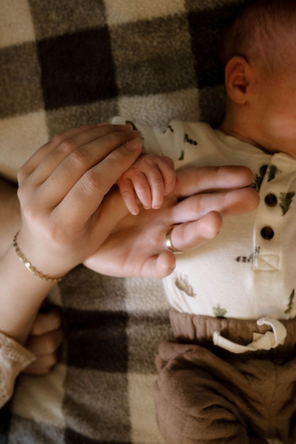 Close-up of hands gently touching on a plaid blanket in warm lighting.