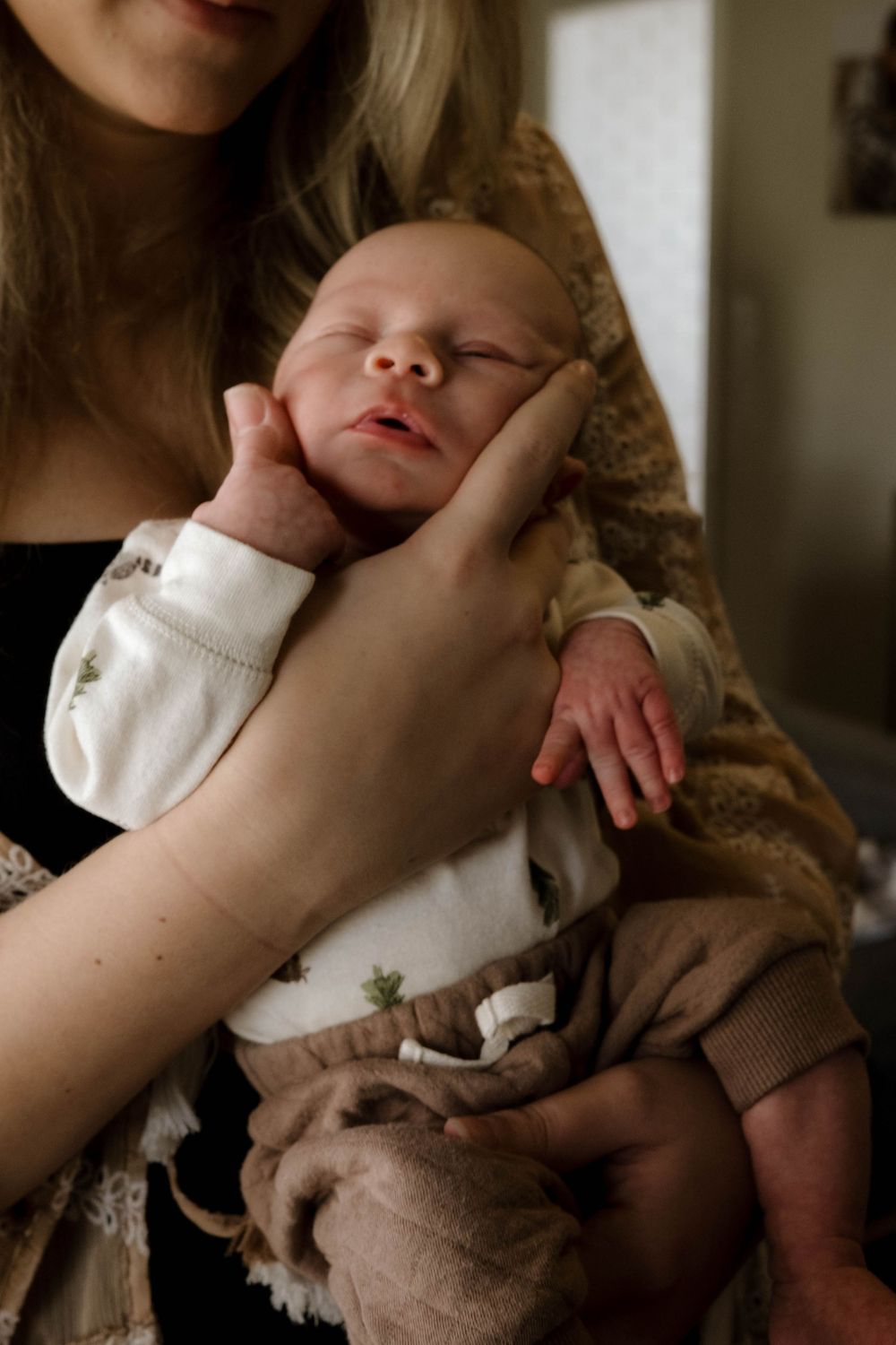 Peaceful sleeping newborn in white onesie being cradled gently.