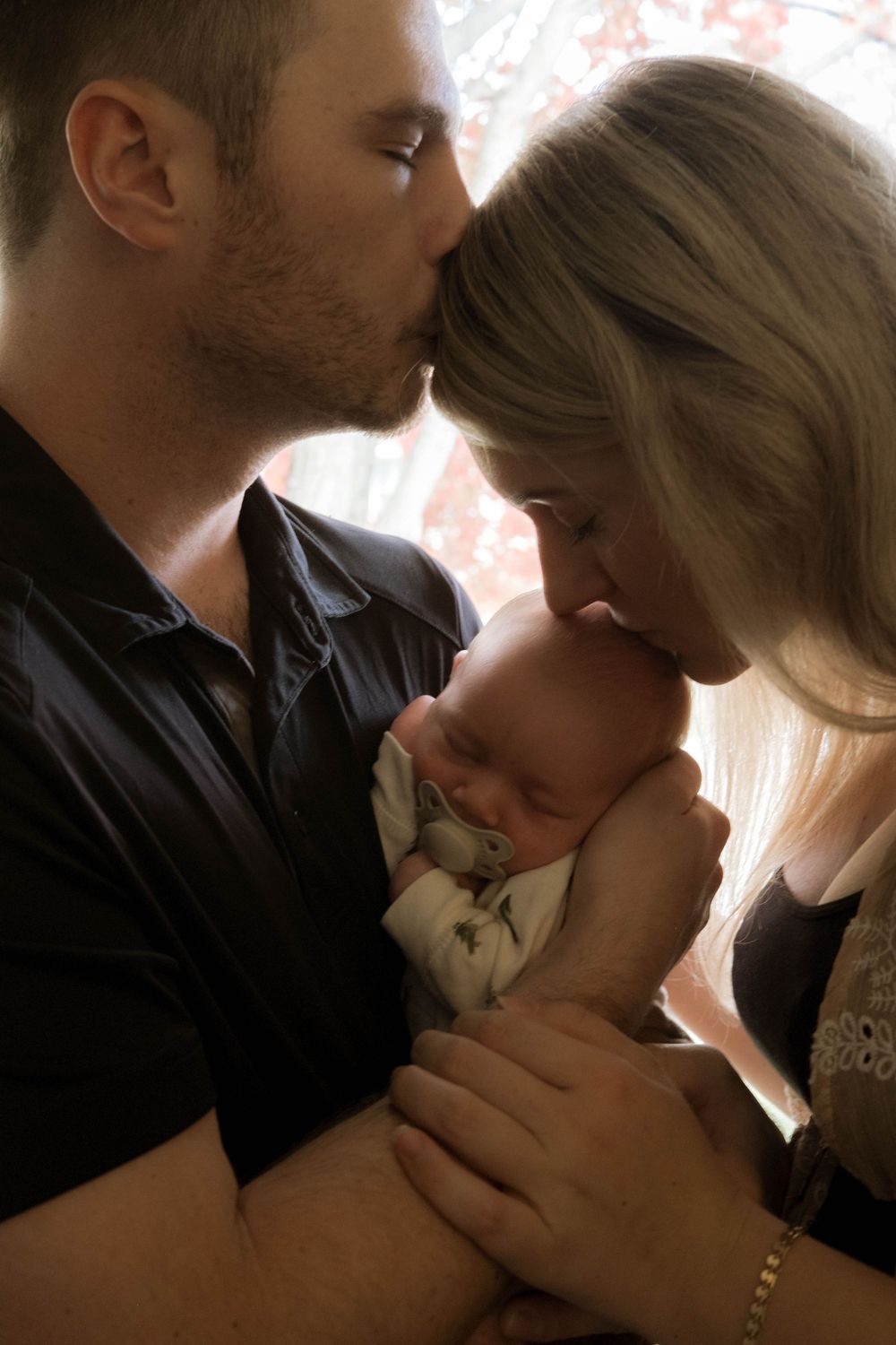 Tender family moment captured in silhouette against window with soft natural lighting.