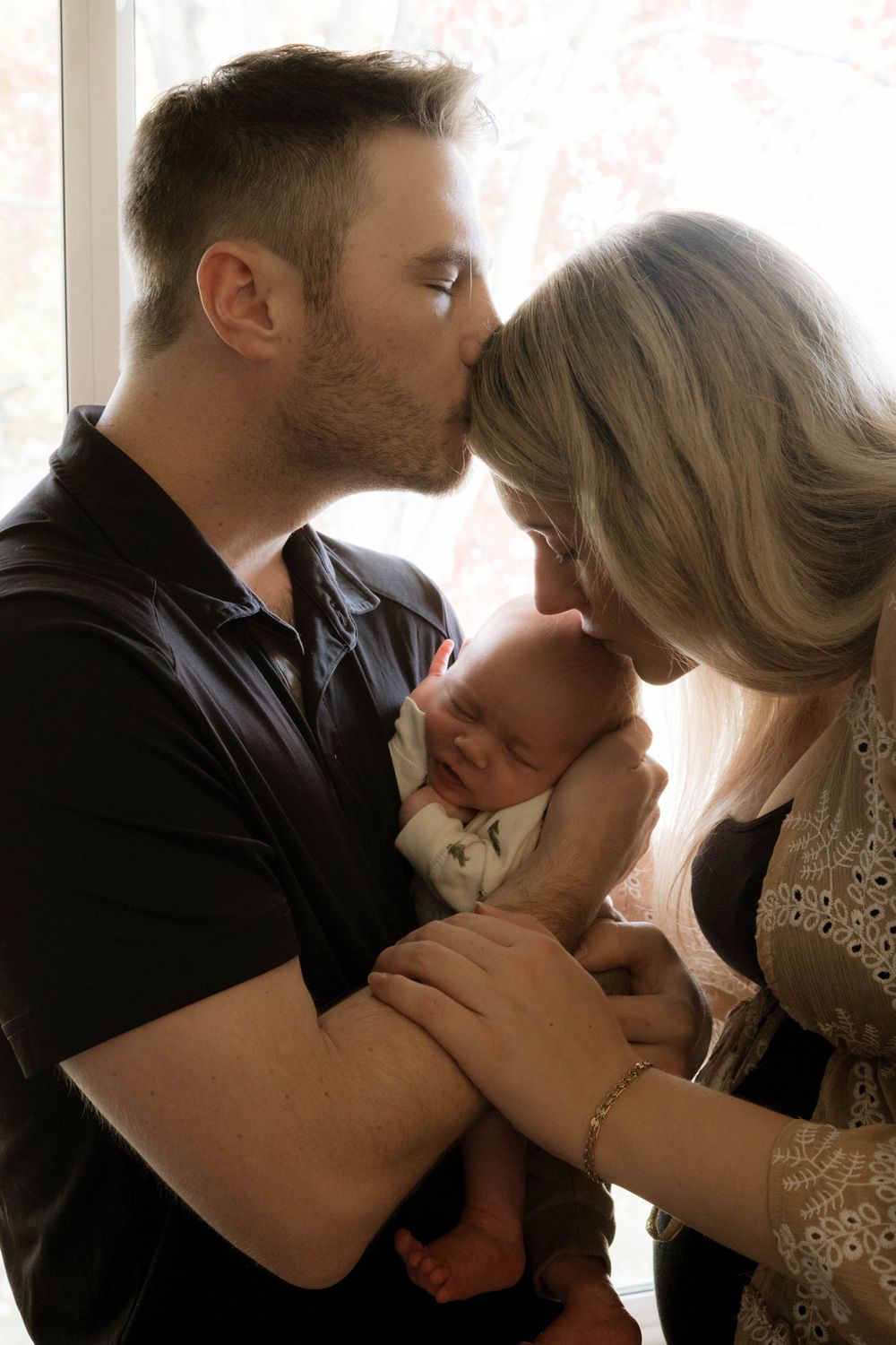 Intimate family portrait with soft window lighting and gentle embraces.