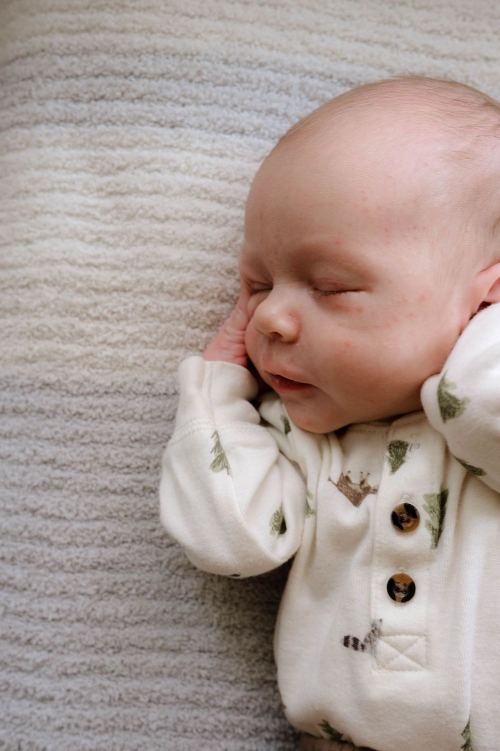 Peaceful sleeping baby in patterned onesie resting on cream textured surface.