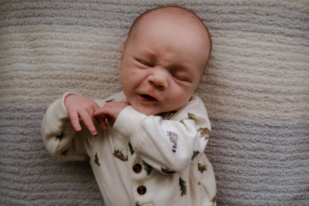 Expressive newborn in woodland-themed onesie on textured light background.
