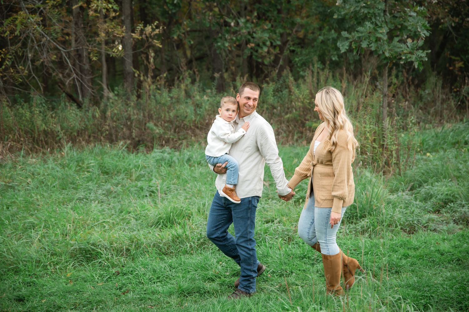 A couple playfully runs through a green meadow on an autumn day, creating a romantic outdoor scene.