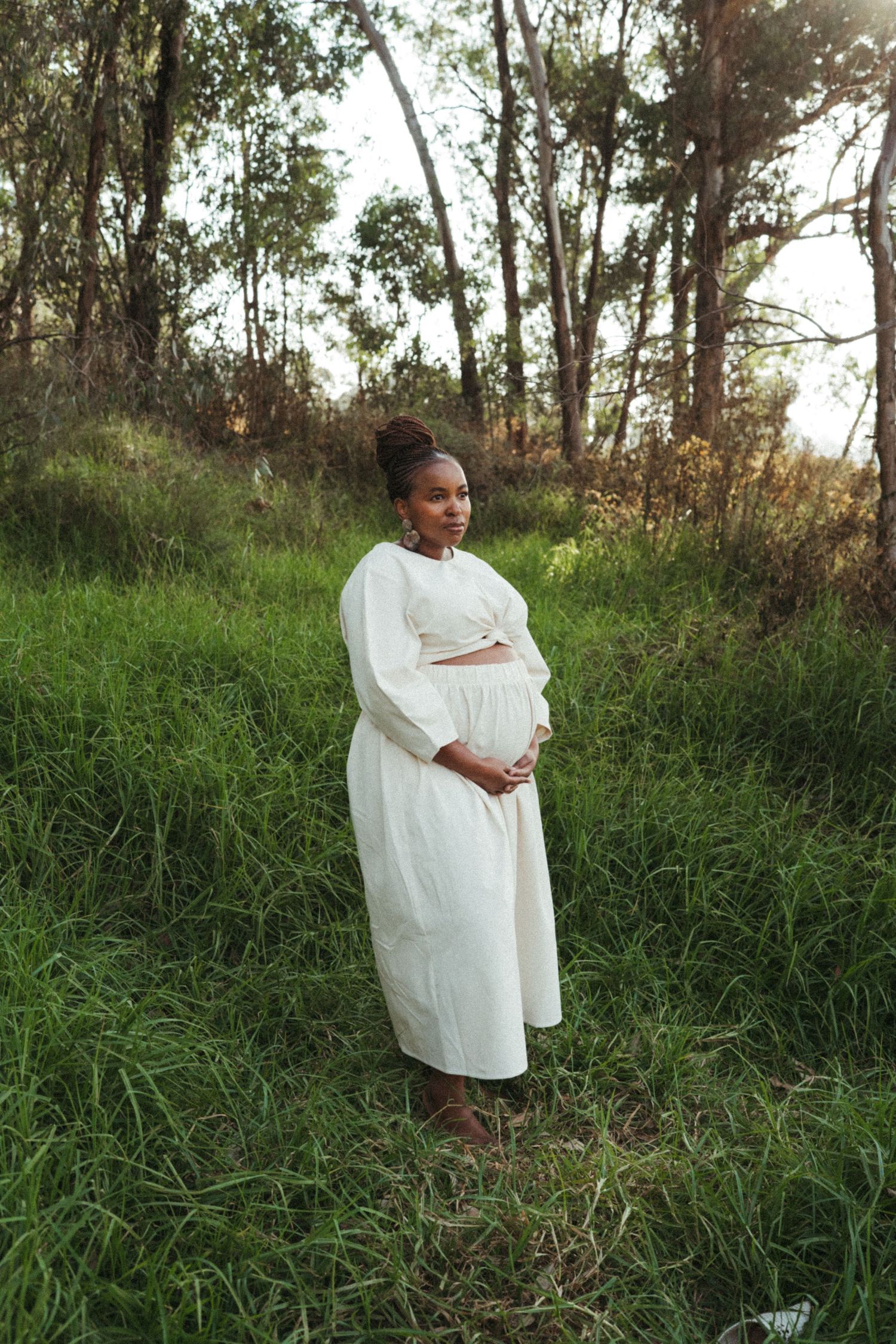 A serene outdoor portrait featuring someone in a white dress against a backdrop of wild grass and trees.