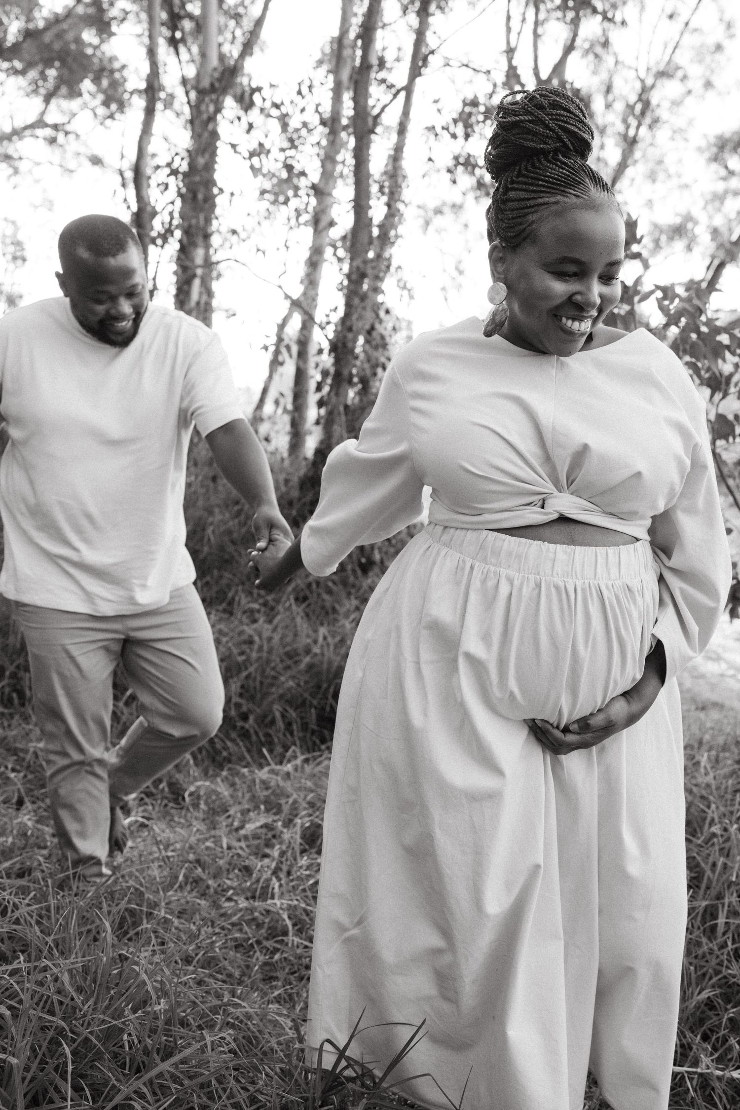 A couple in white outfits embracing and laughing together in a natural outdoor setting.