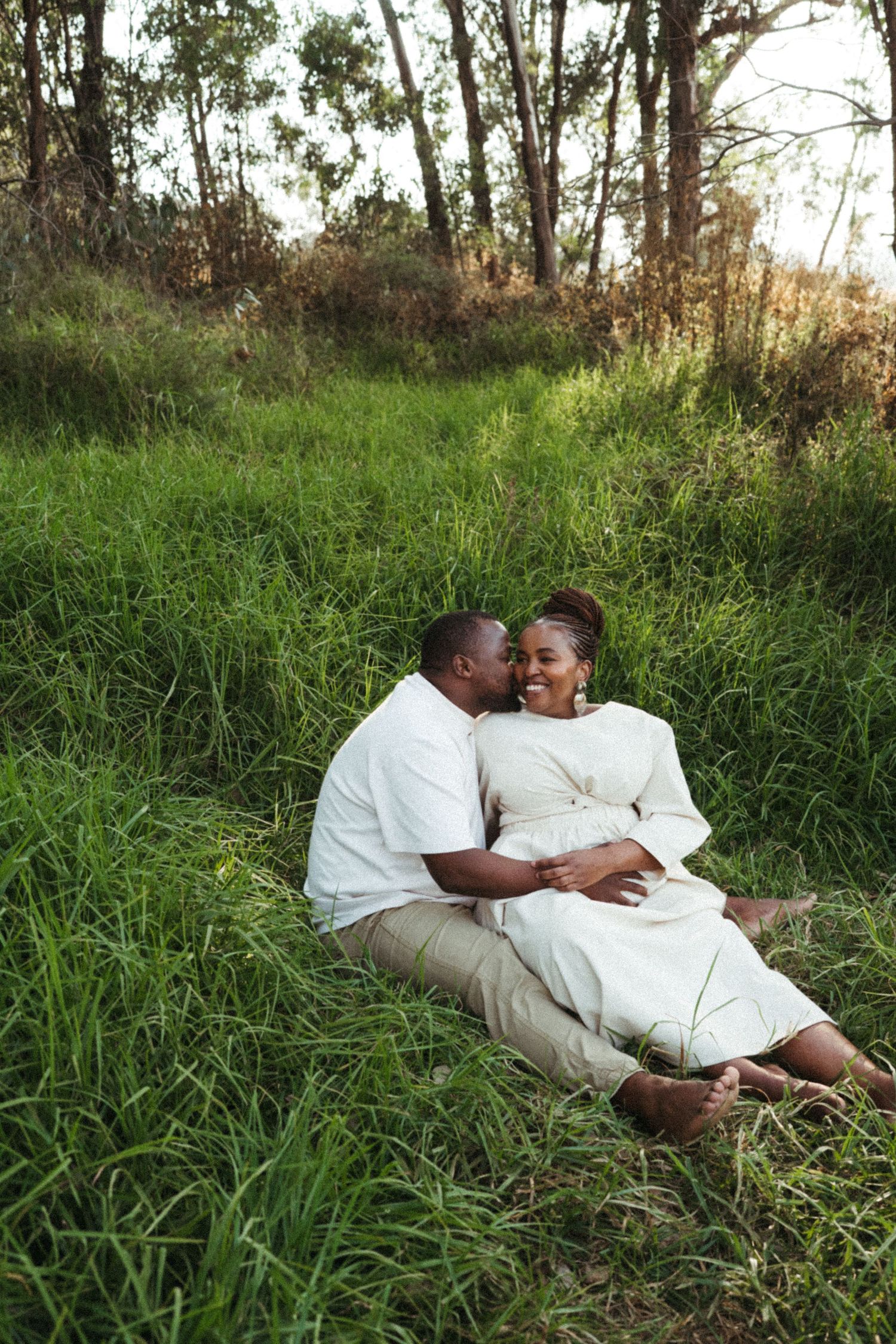 A romantic couple lying together in tall grass during a sunny outdoor photoshoot.