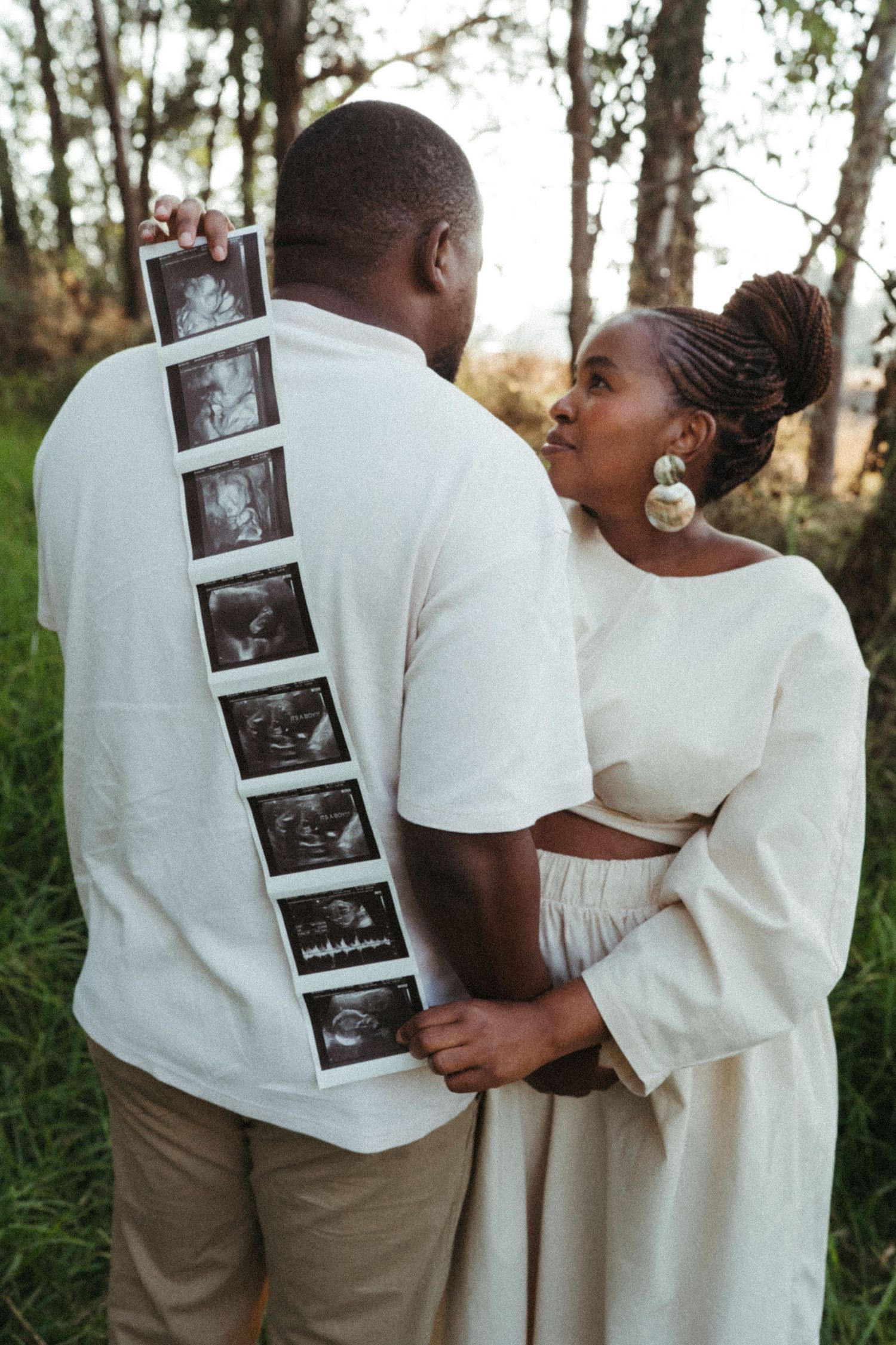 Couple in white clothing holding ultrasound photos during pregnancy announcement photoshoot.