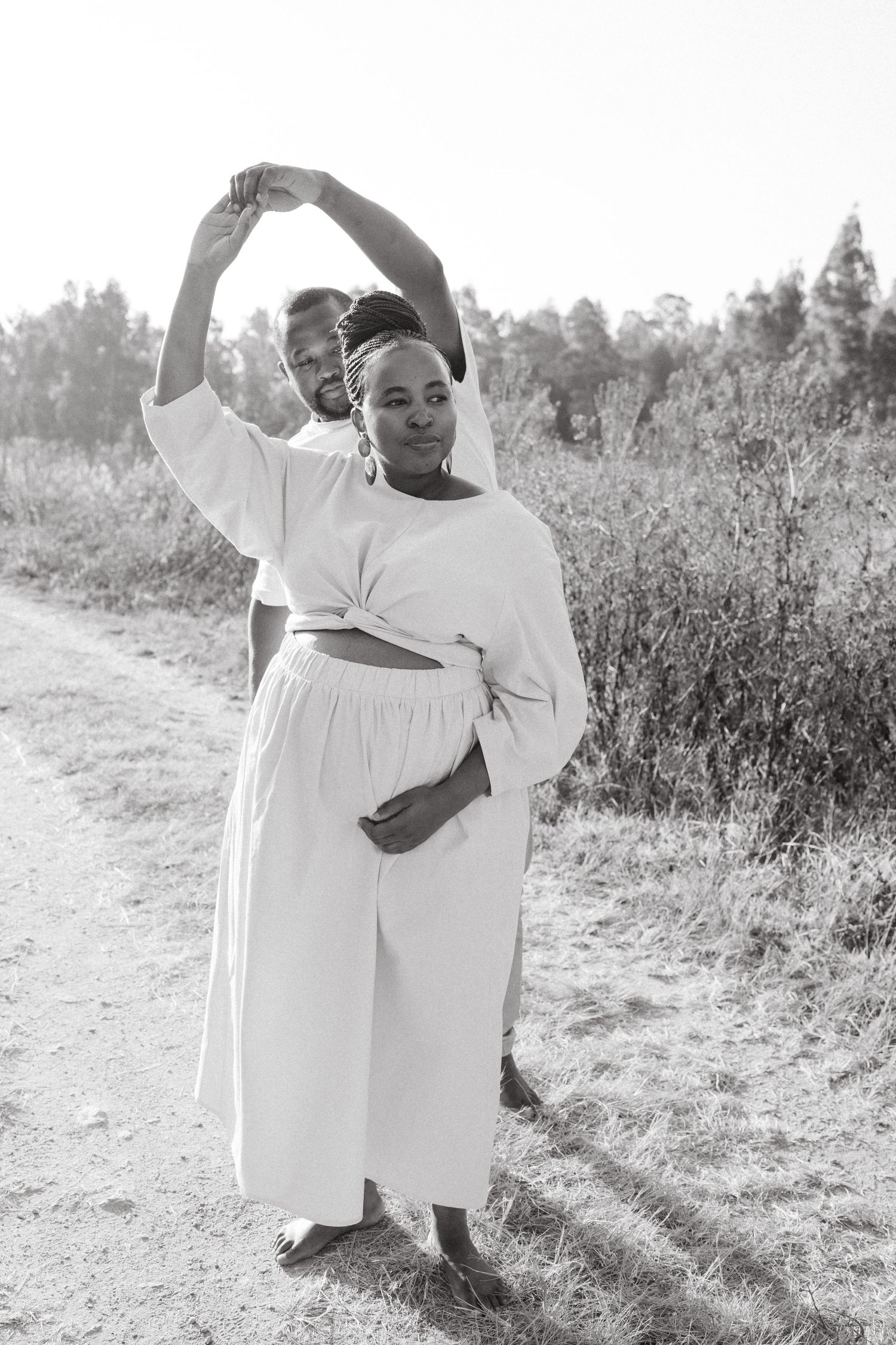 Joyful couple in white outfits dancing and celebrating in a sunny outdoor field.