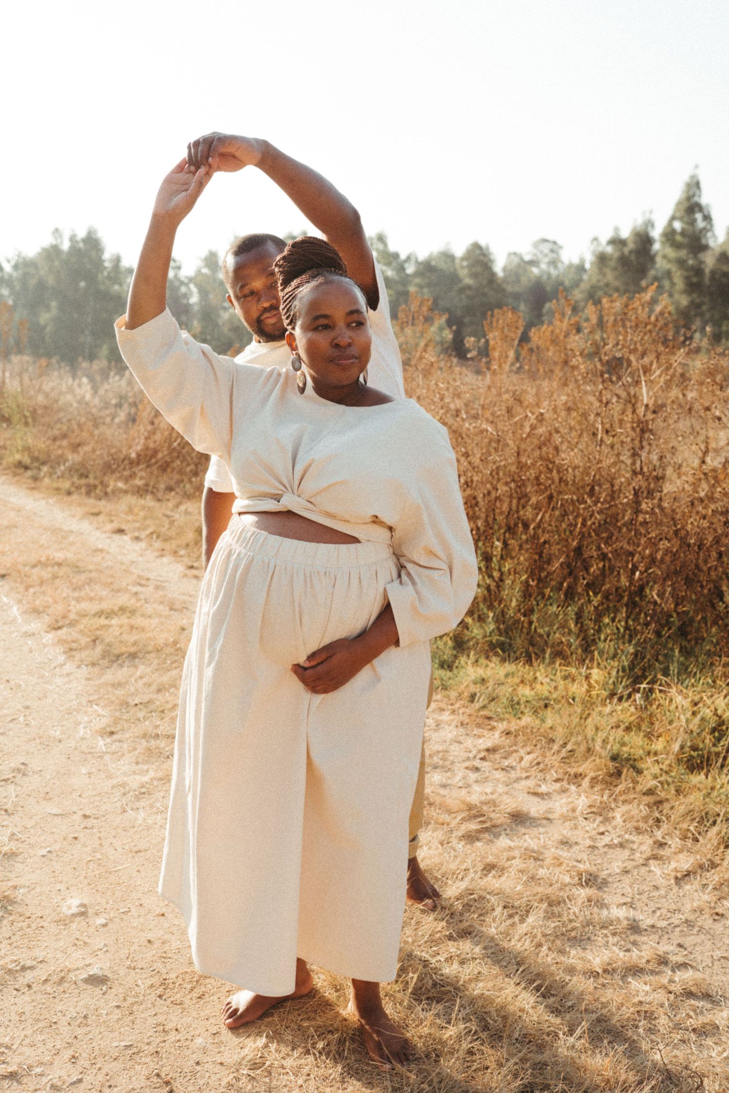Happy couple in white clothing dancing and celebrating together in golden sunlight.
