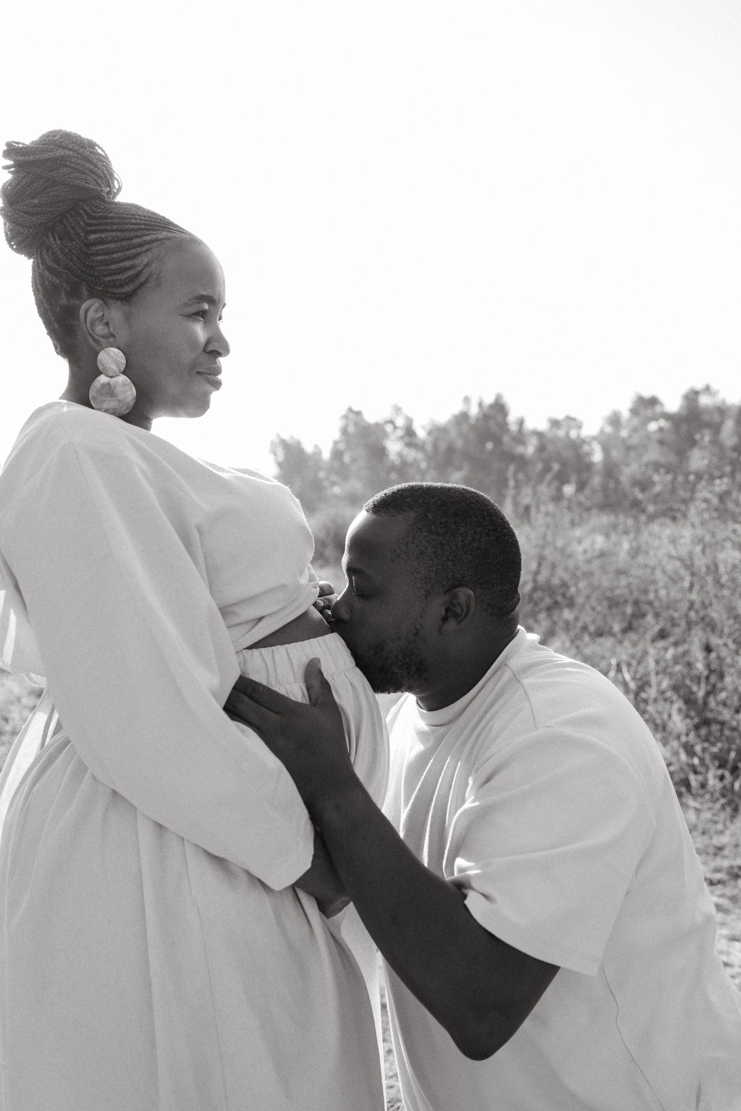 Intimate black and white maternity photo showing a tender moment between expectant parents outdoors.