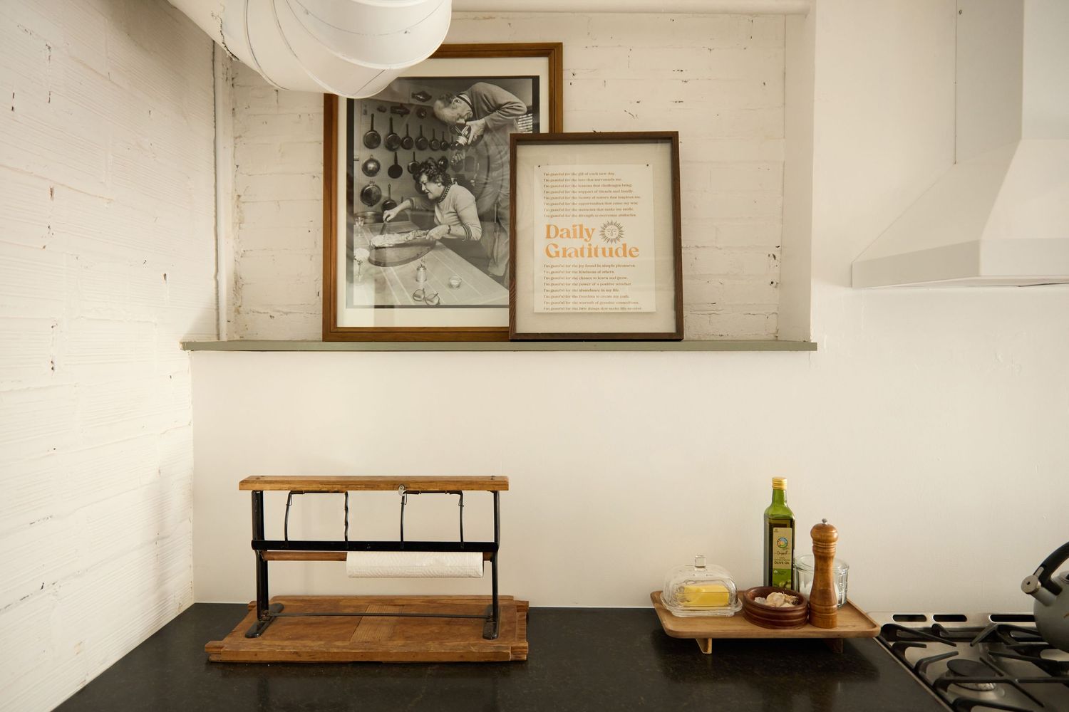 Minimalist kitchen shelf with framed artwork, wooden cutting board, and wine bottles on black countertop.