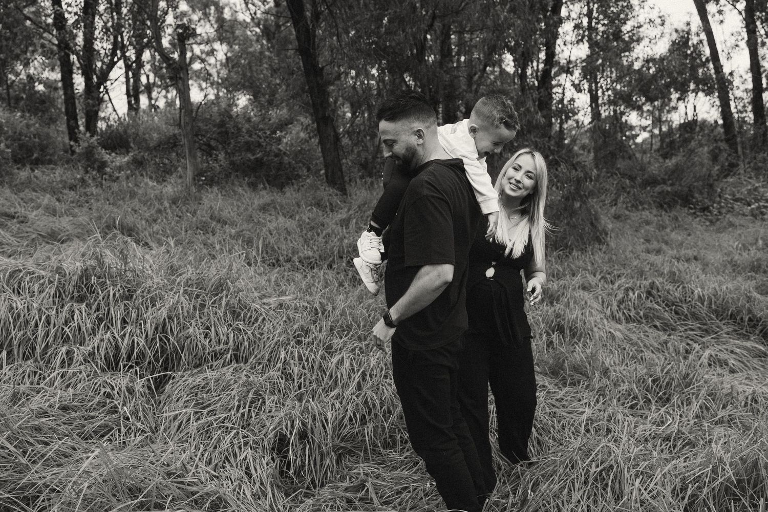 A couple shares a joyful moment together on a grassy hillside surrounded by trees.