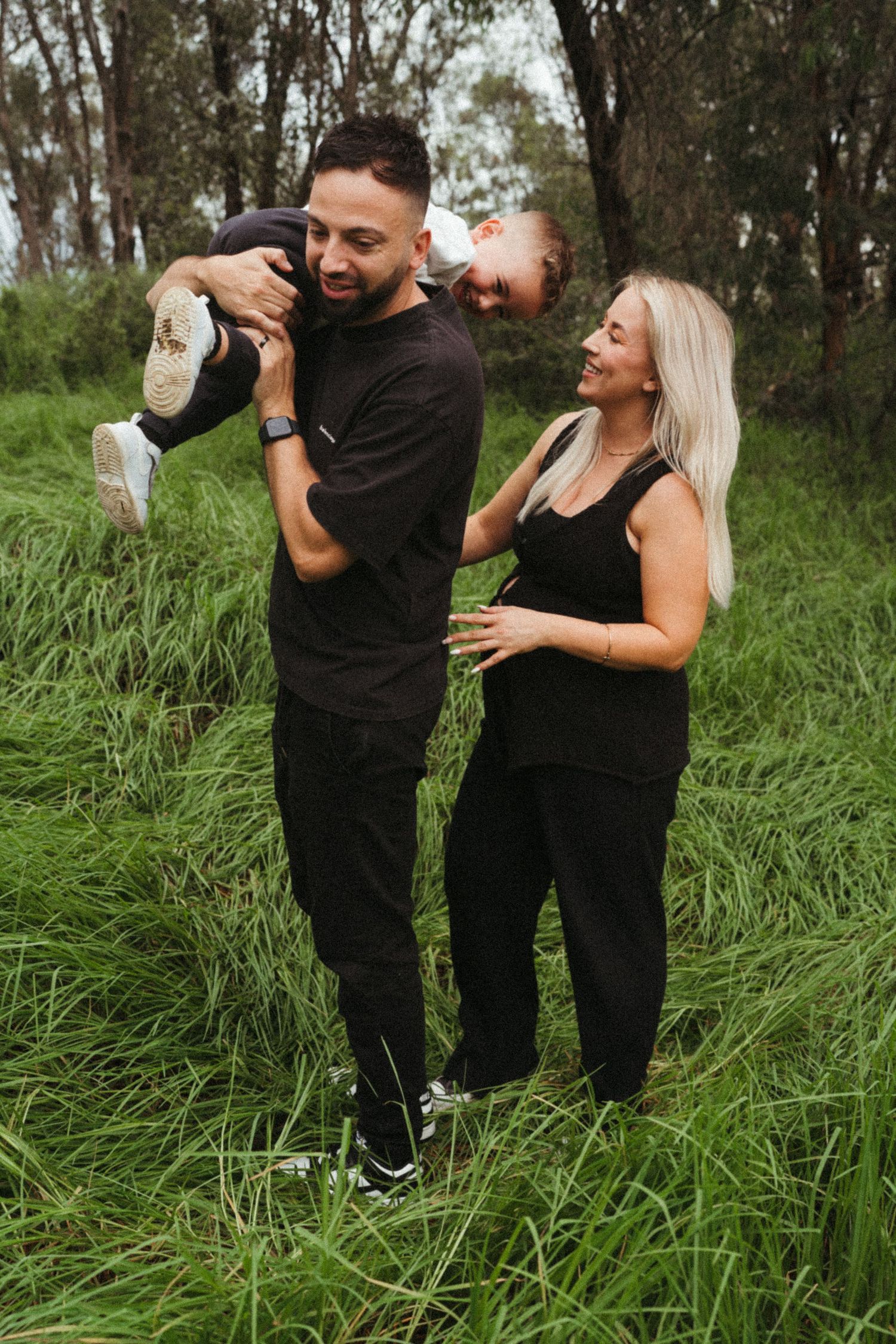 Couple sharing joyful moments together in tall grass with trees in background.