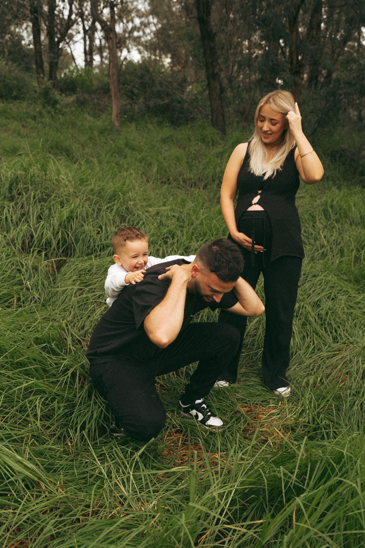 Two people in black clothing sharing candid moments in a grassy field.
