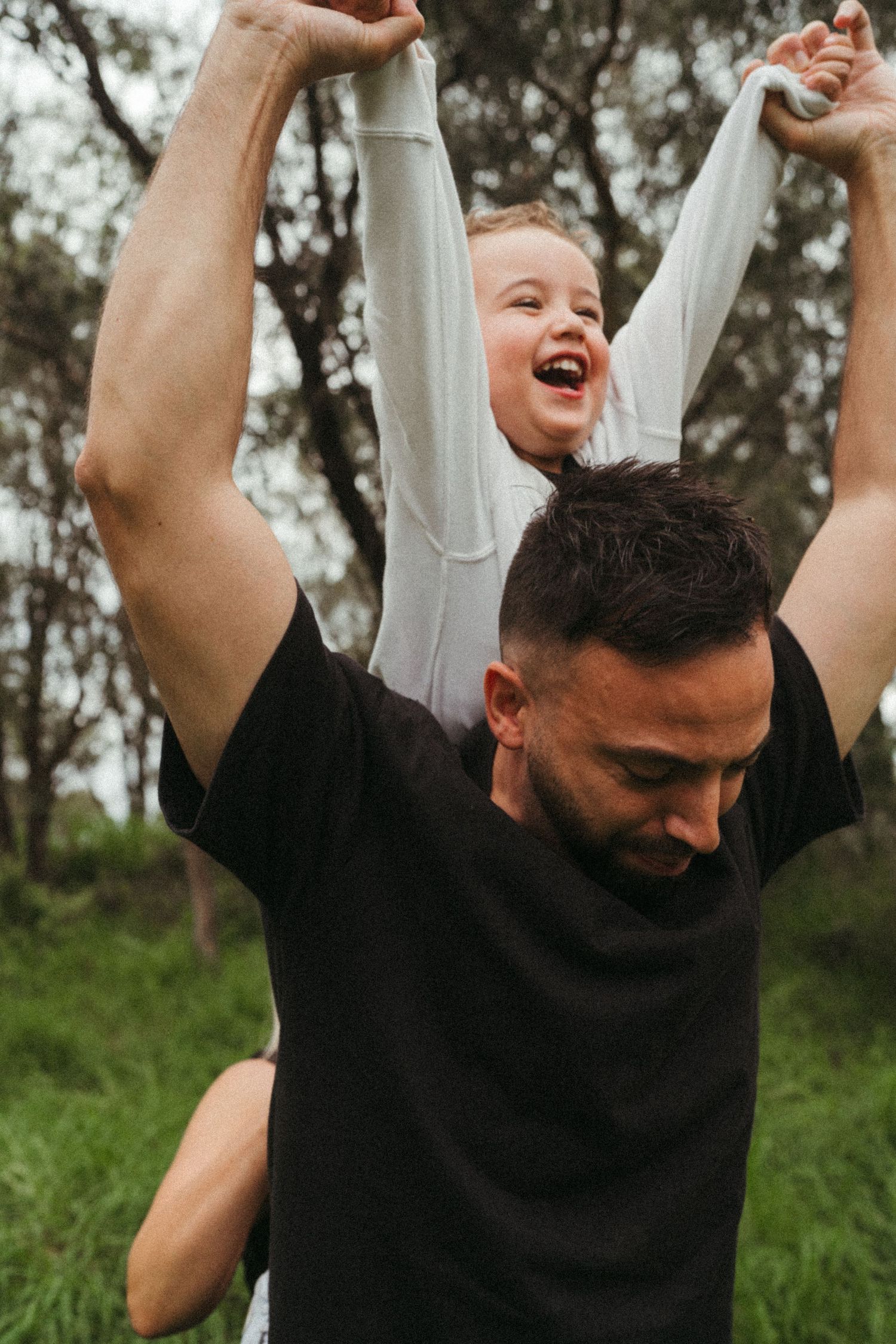 Person in black shirt celebrating with arms raised in an outdoor setting.