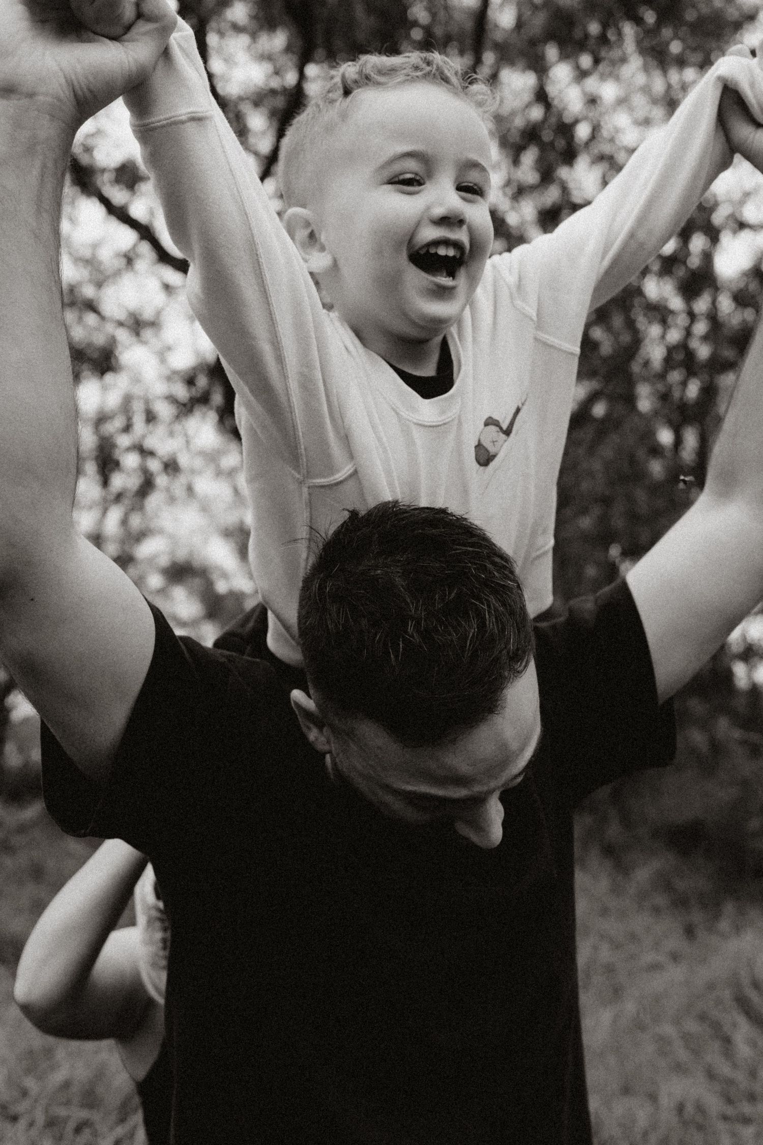 Black and white image of joyful celebration with raised arms against trees.