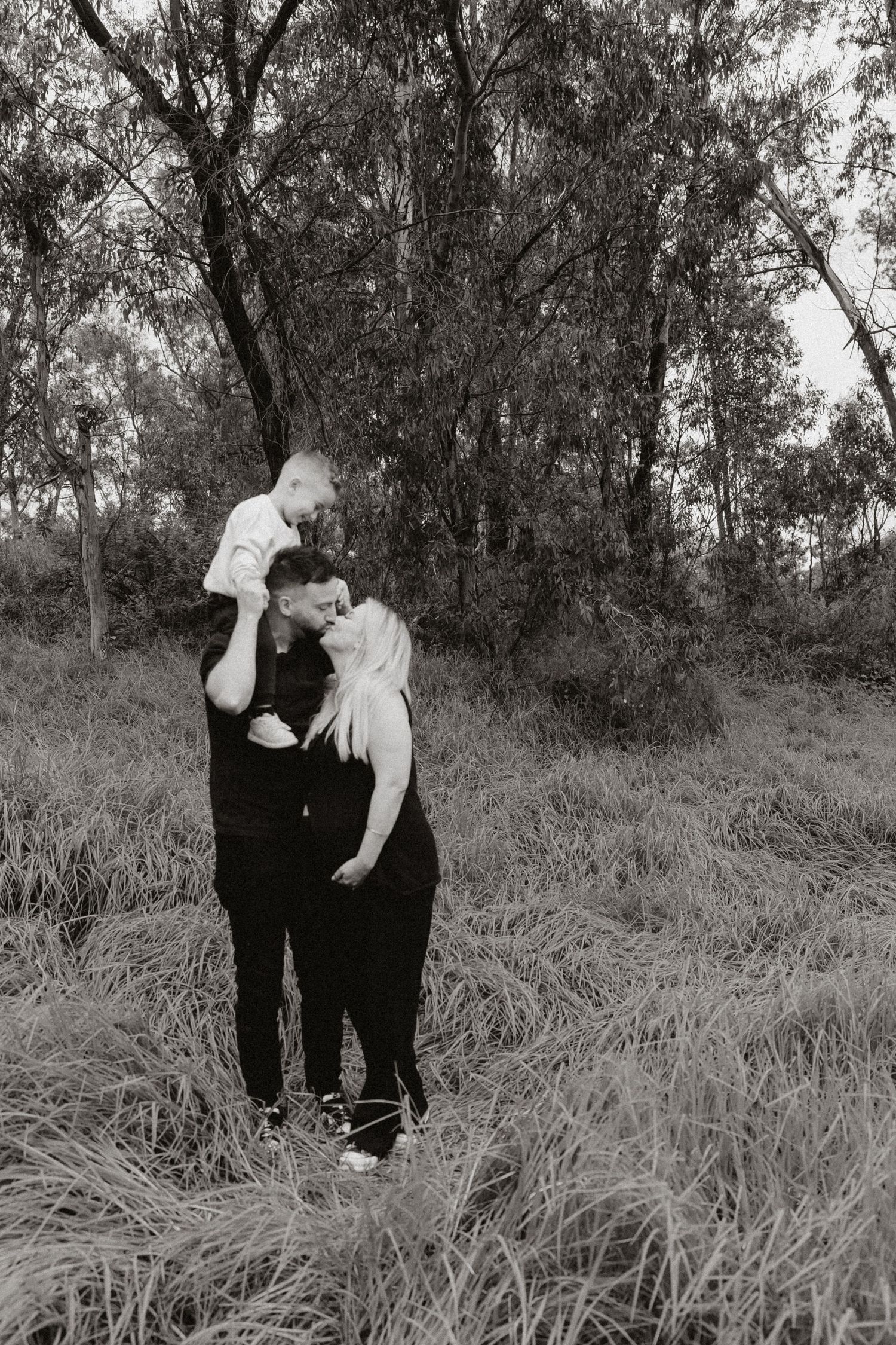 Two people sharing a tender moment together in a grassy field with trees in the background.