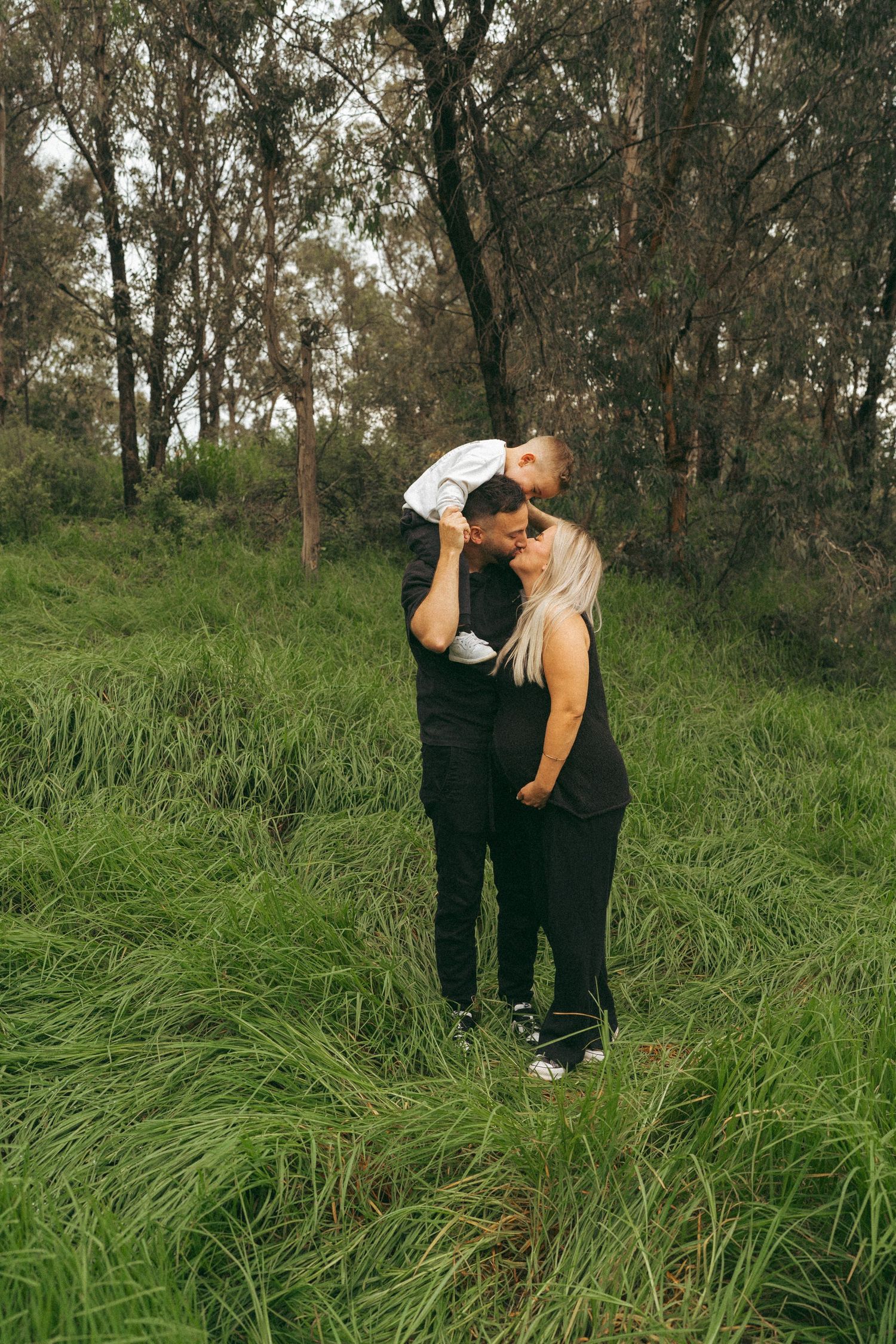 A couple interacting playfully in tall grass with eucalyptus trees behind them.