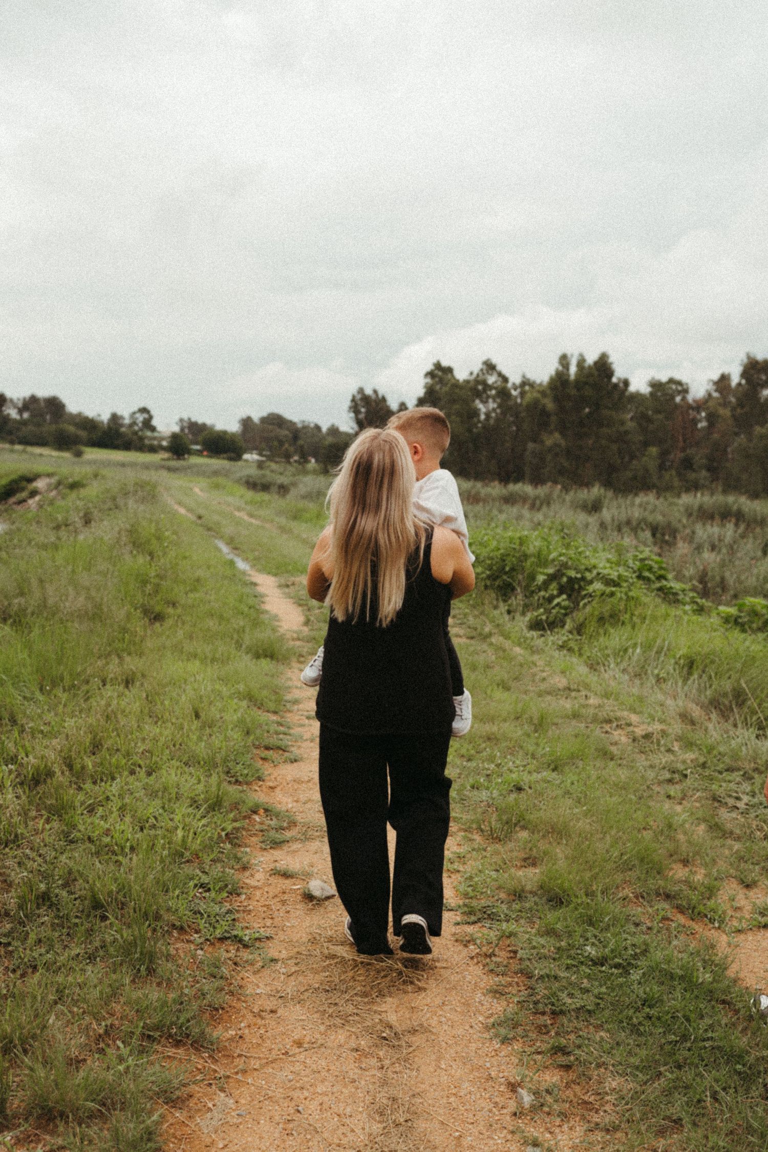 Two people walking together on a winding dirt path through a grassy field.