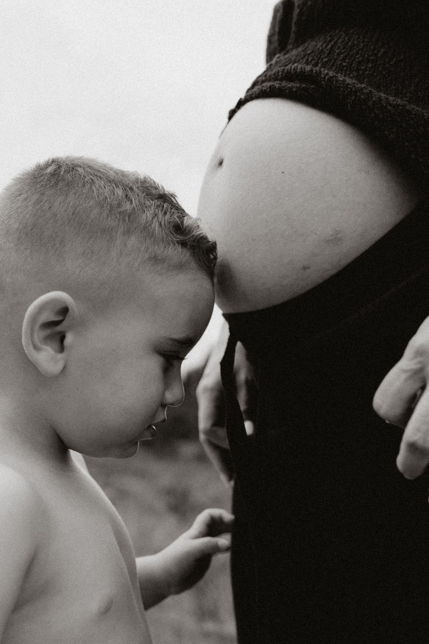 A tender black and white photo showing a young child gently touching a pregnant belly.