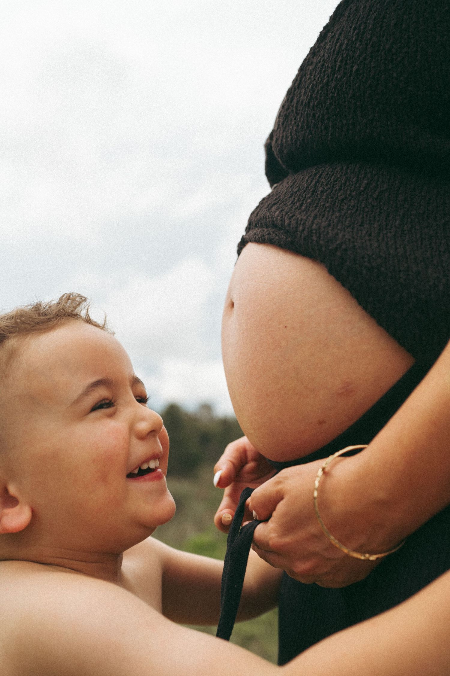 A joyful moment captured between a small child and an expectant mother's belly outdoors.