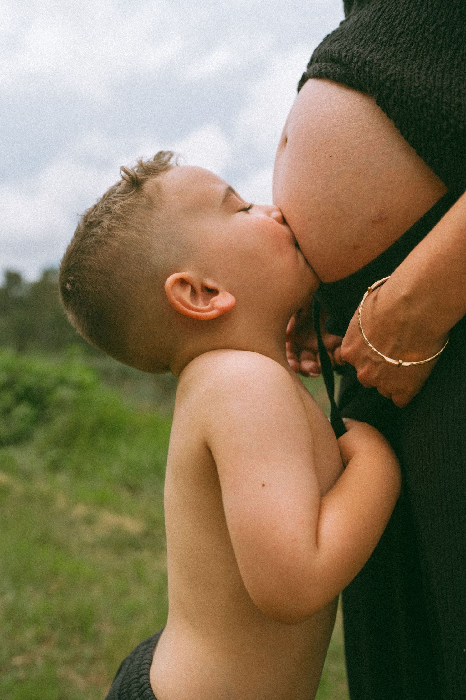 An intimate moment showing a child kissing a pregnant belly while holding onto clothing.