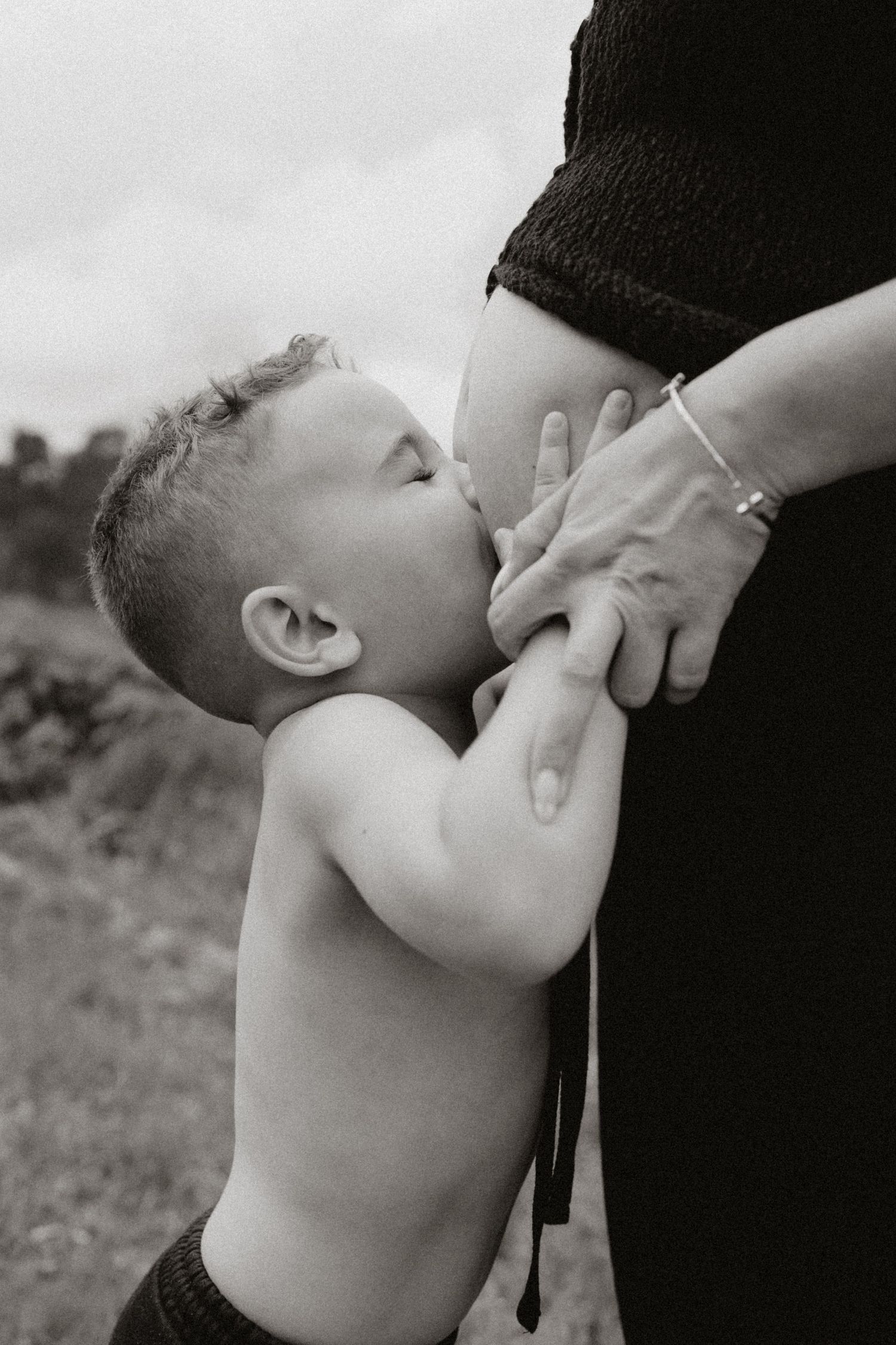 An emotional black and white photograph of a child reaching up to touch a pregnant belly.