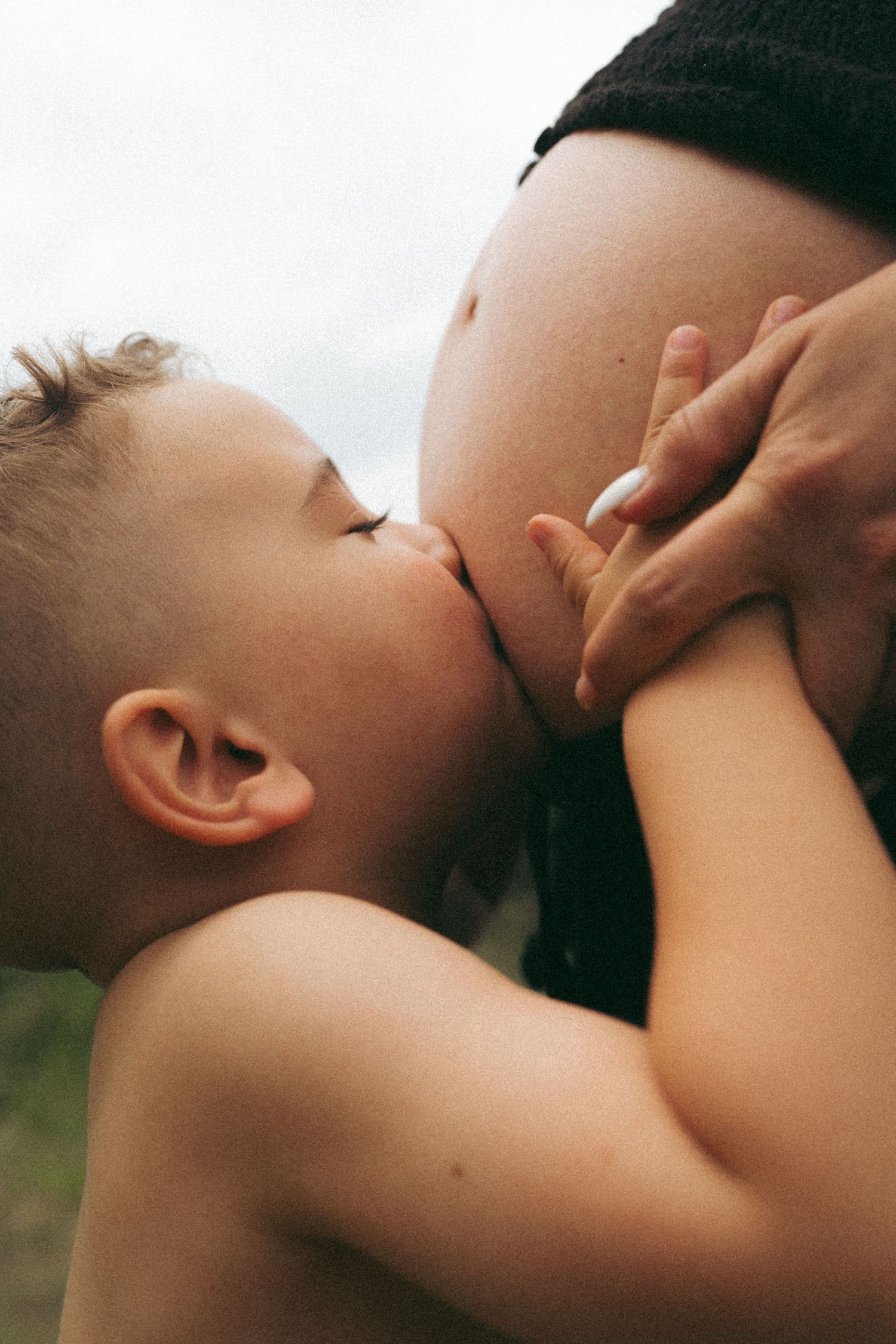 A close-up photo capturing an intimate moment between a child and a pregnant belly.
