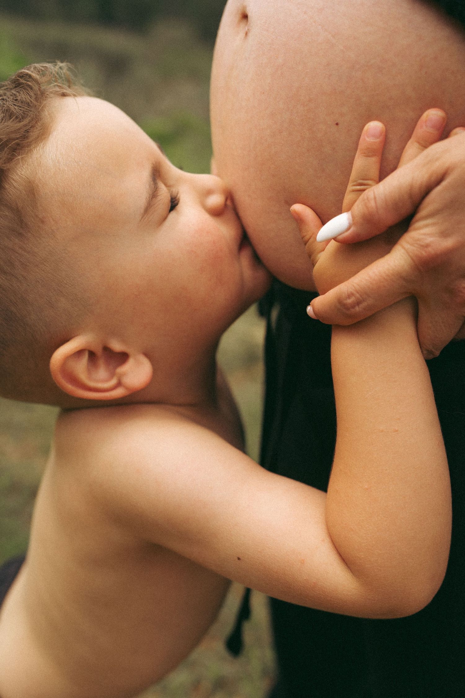 A touching moment showing a child kissing a pregnant belly in warm natural light.
