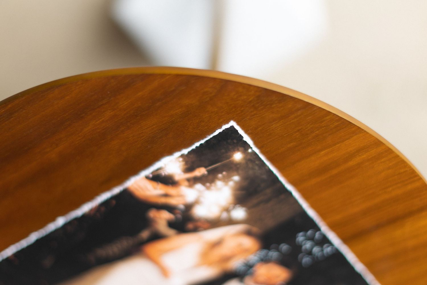 A stack of old photographs fanned out on a wooden table surface in warm lighting.