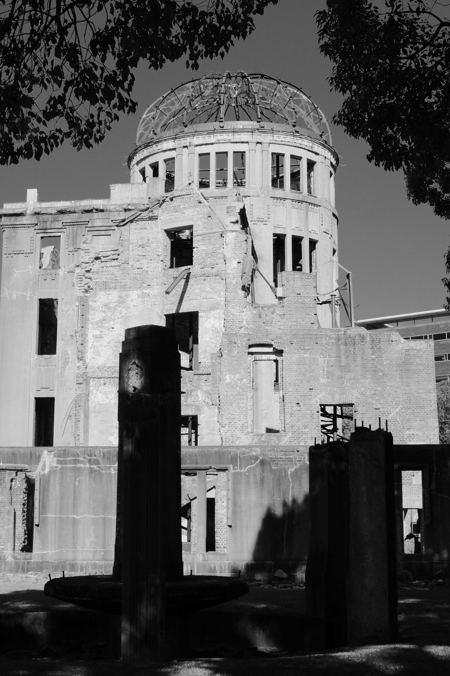 The historic Atomic Bomb Dome in Hiroshima stands as a preserved ruin against a blue sky, framed by green trees.