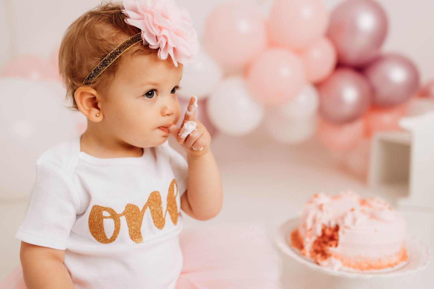 Pink and gold cake smash photo session setup with balloons and decorations for a first birthday celebration.