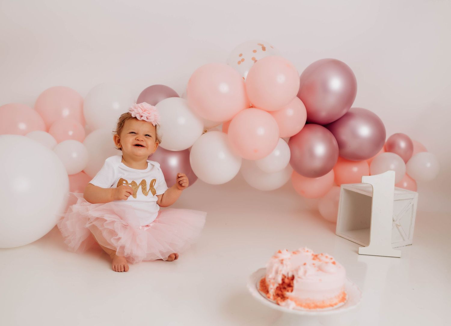Pink and silver balloon arch decorates a baby's first birthday cake smash photo session with soft pastel colors.