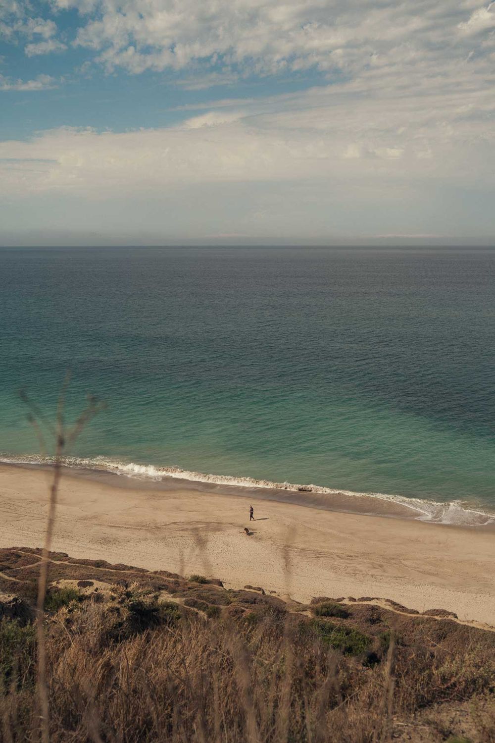 Panoramic aerial view of a pristine sandy beach with turquoise ocean waters and dramatic cliffs along the coastline.