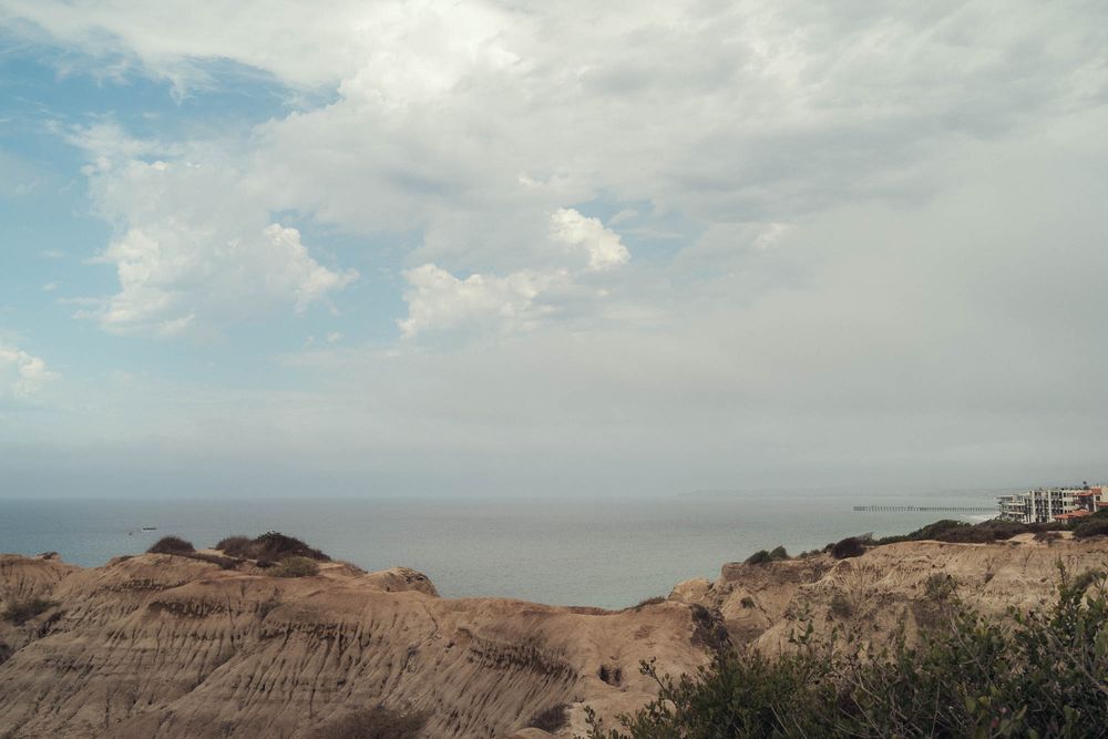 Desert landscape with rugged mountains and rocky terrain under cloudy skies stretches into the distance.