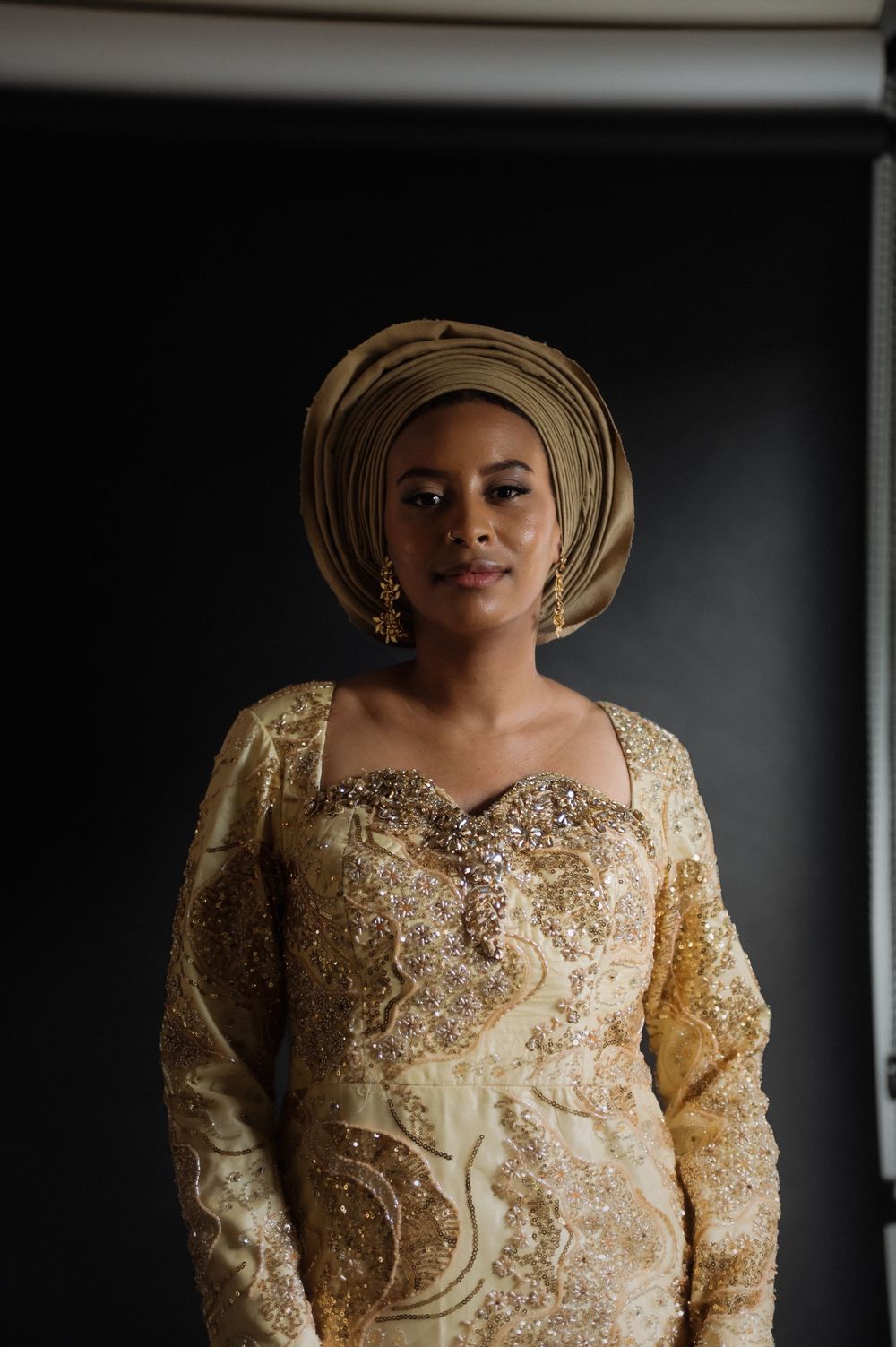 Elegant gold beaded dress with traditional headwrap photographed against dark background.