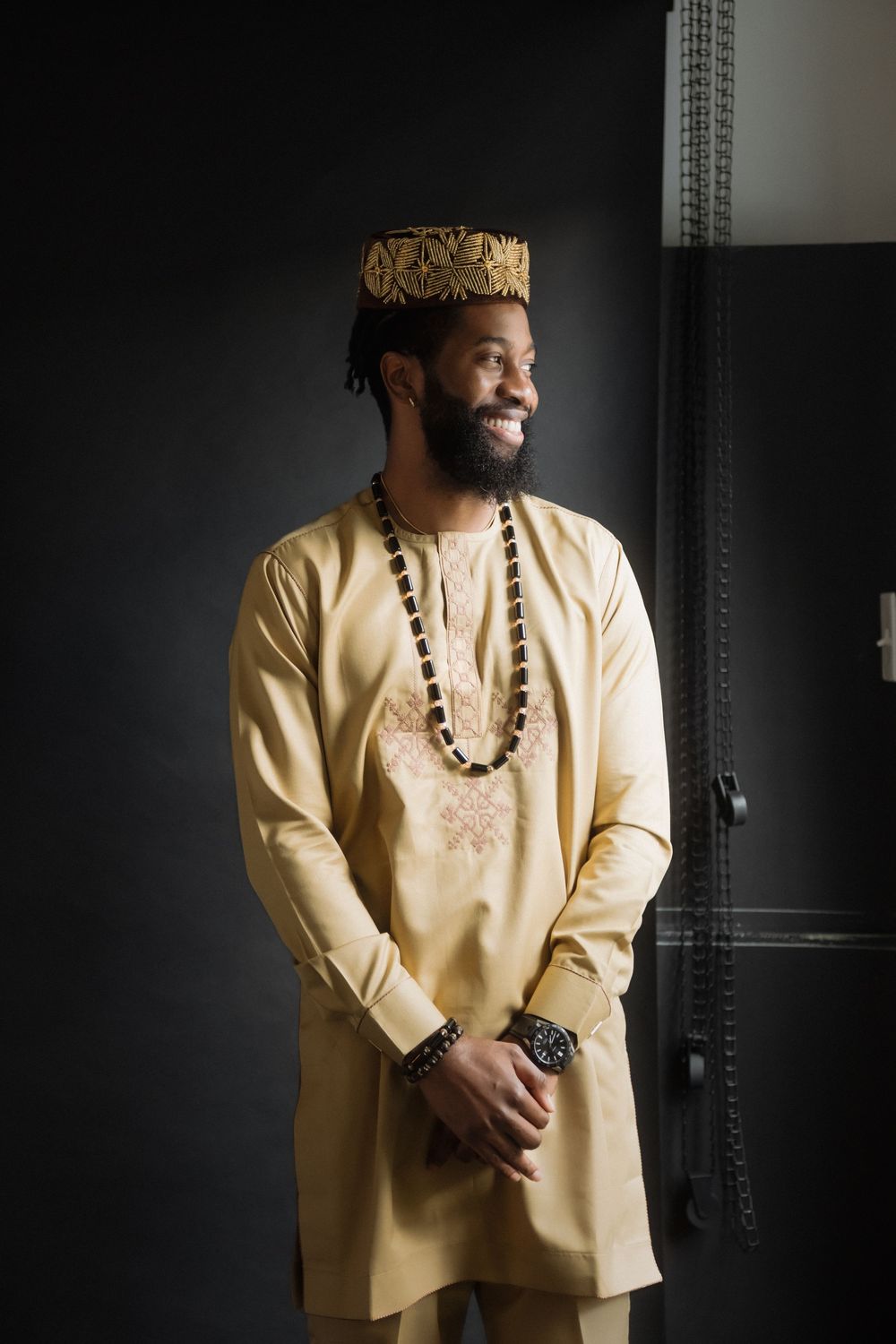 Traditional cream agbada with beaded necklace photographed against dark background.