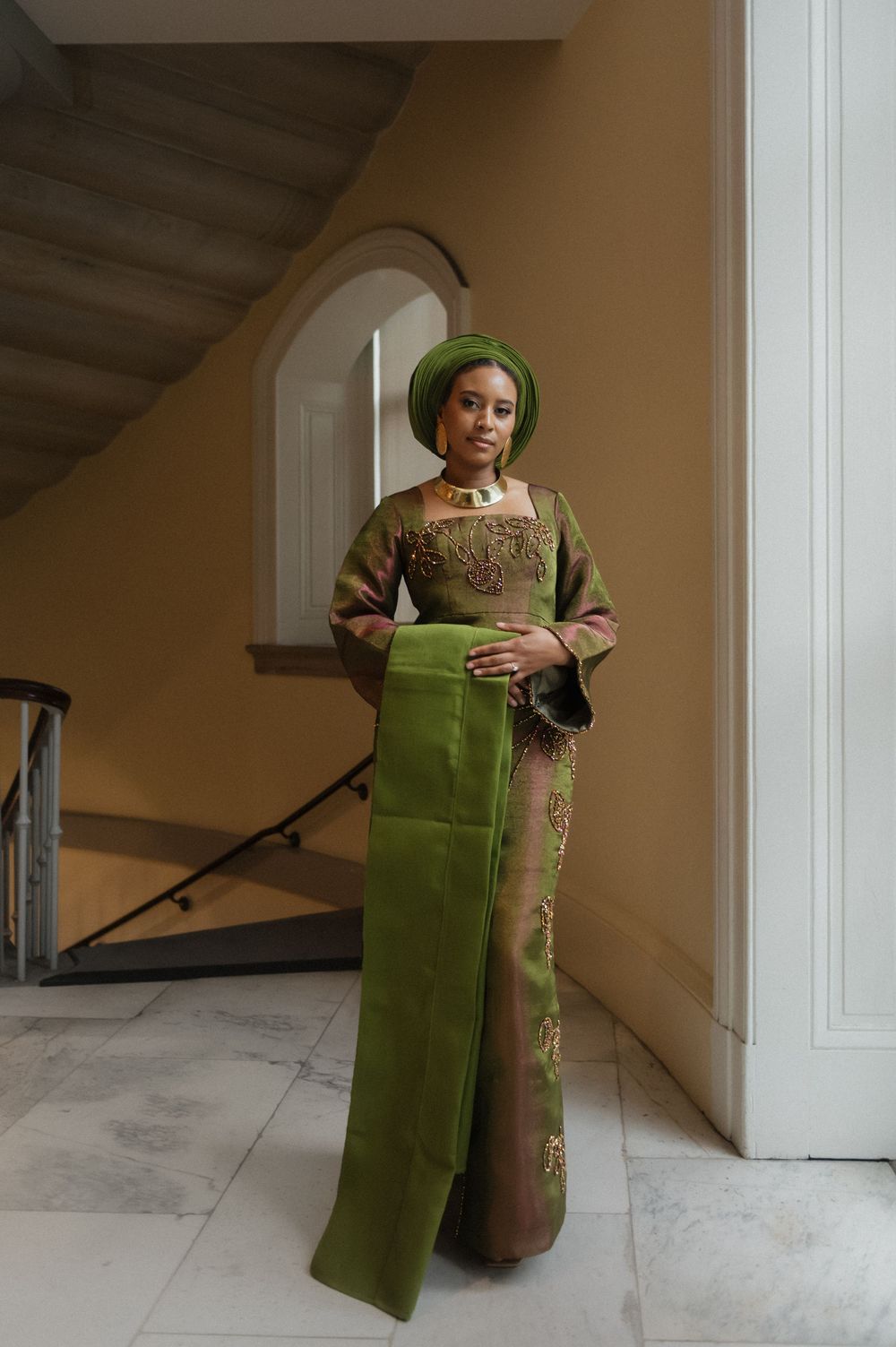 Person in green traditional dress holding matching fabric panel in sunlit room.