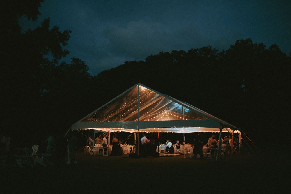 A glowing wedding tent illuminated at night with guests gathered underneath during an outdoor reception celebration.