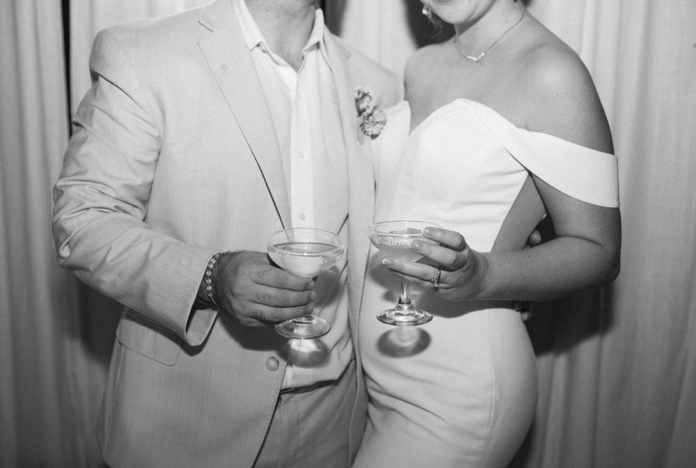 People in white formal attire holding drinks and socializing at an elegant party gathering.