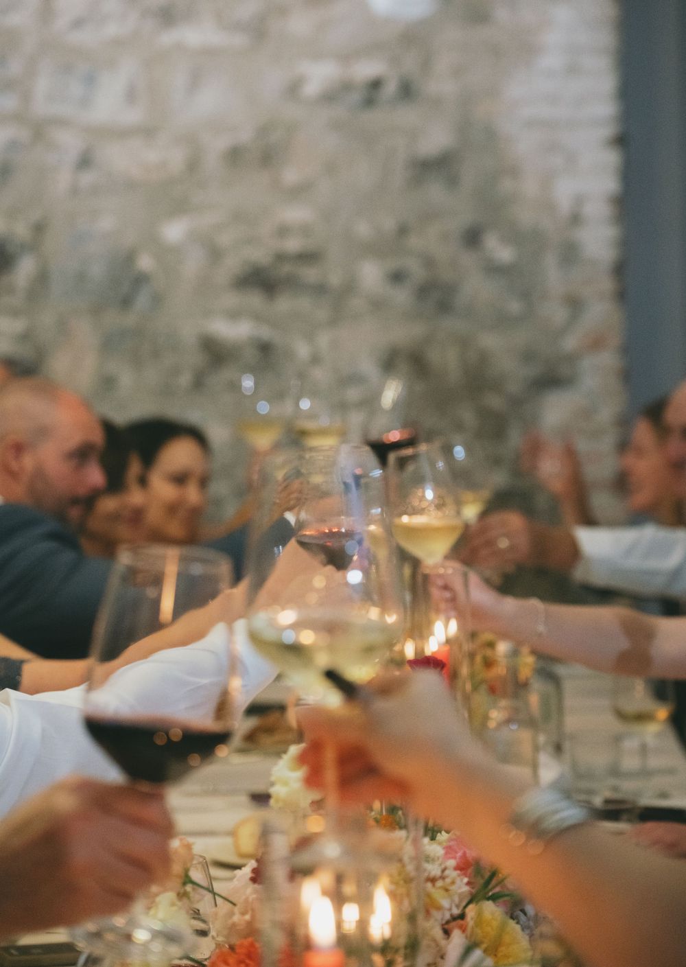 Guests raise wine glasses in a candlelit toast during an intimate dinner gathering.
